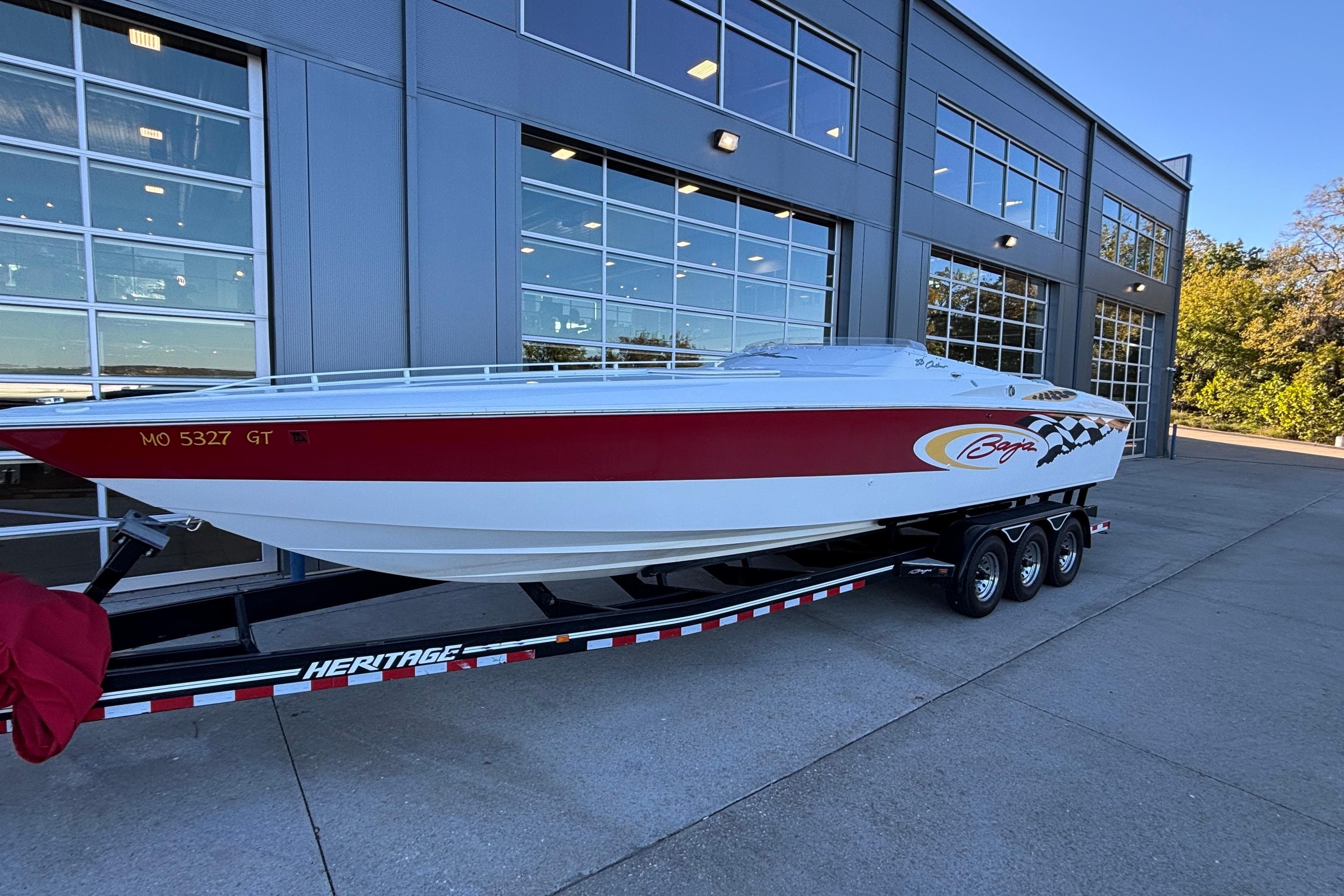 2001 Baja 33 Outlaw speedboat on trailer, parked outside a modern building.