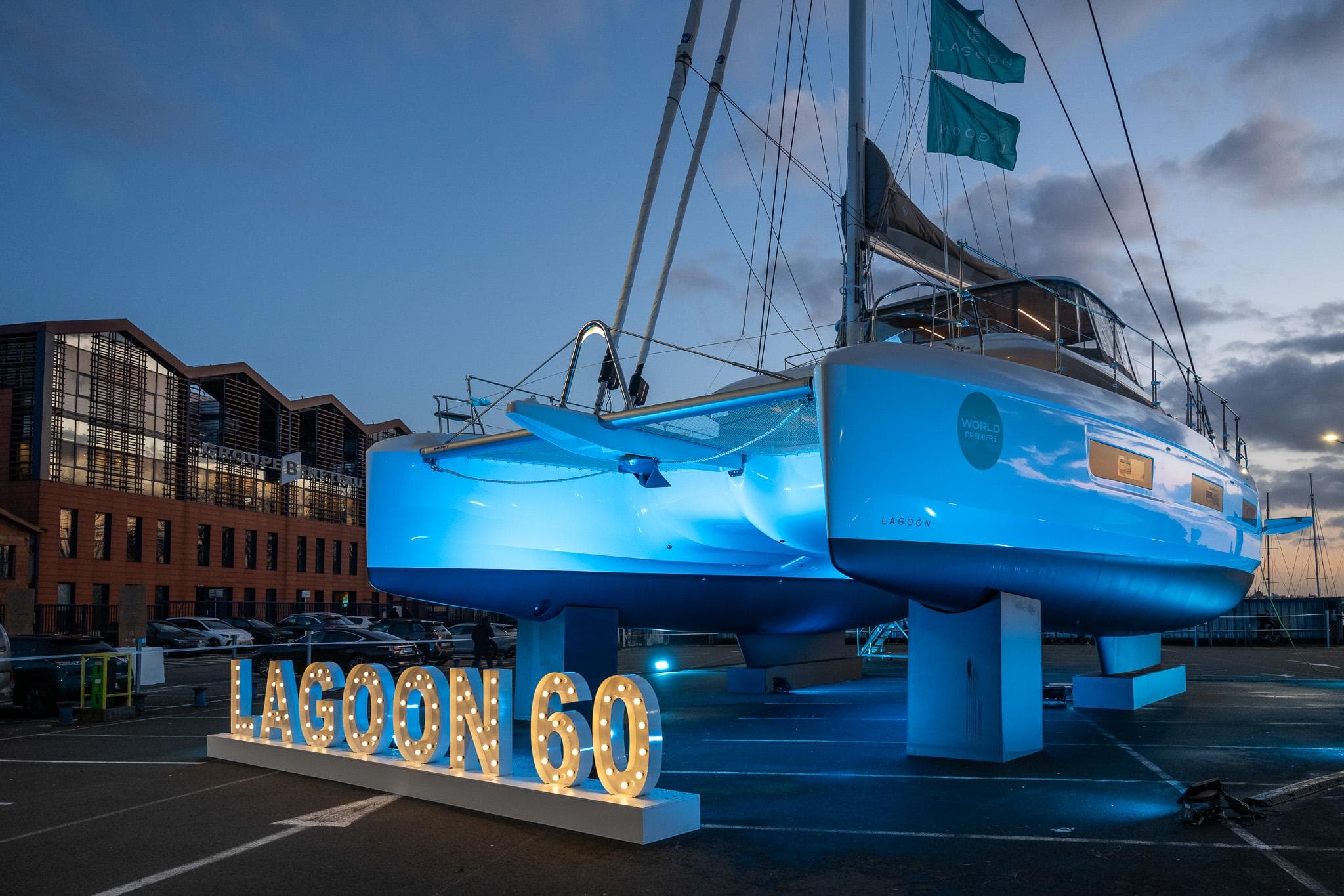 2025 Lagoon 60 yacht displayed at dusk with illuminated sign.