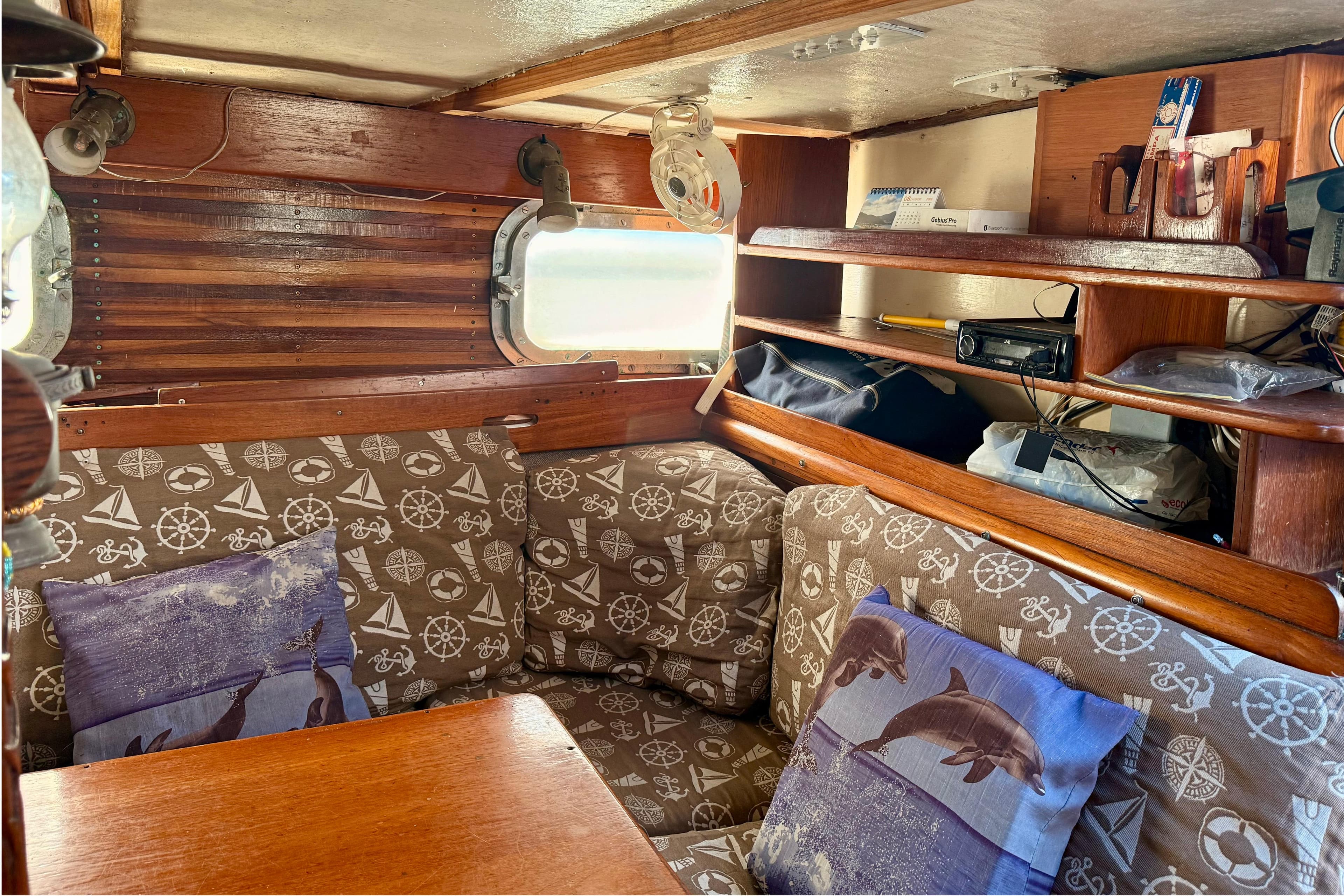 Interior of 1966 Cheoy Lee Gulf 40 sailboat with nautical-themed cushions and wooden shelves.