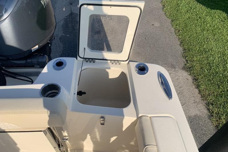 2026 Scout 215 XSF boat with open storage compartment and motor, parked on pavement.