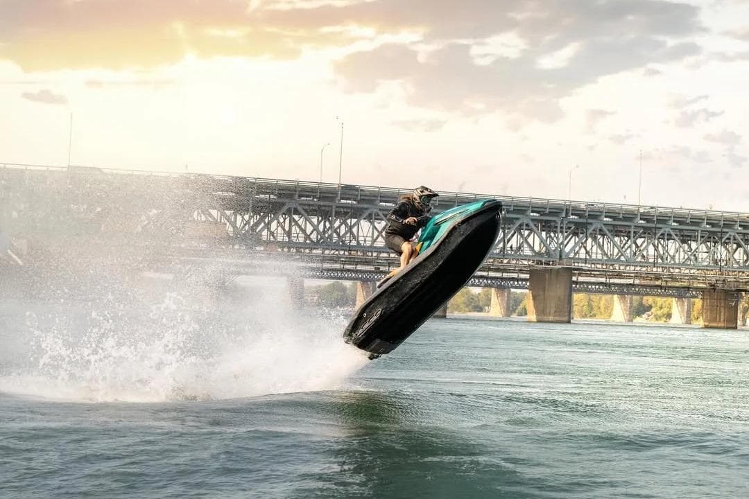 Person riding 2025 Taiga Orca P2 jet ski, jumping over water near a bridge.