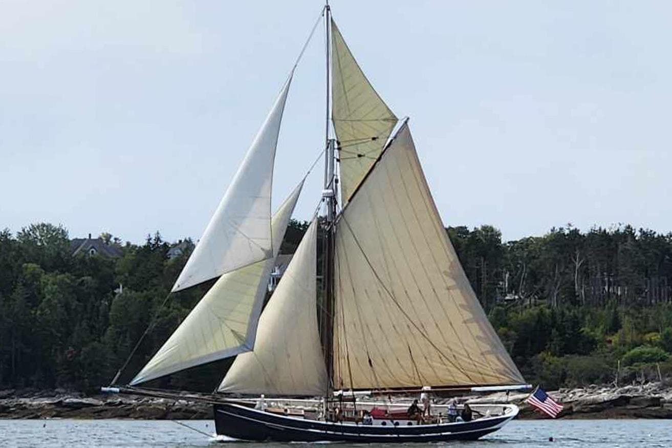 Custom 2004 Luke Powell Pilot Cutter sailing near forested shoreline.
