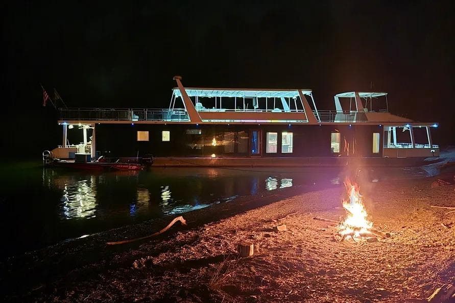 Houseboat Thoroughbred 21x103, 2012 model, illuminated at night by a lakeside campfire.