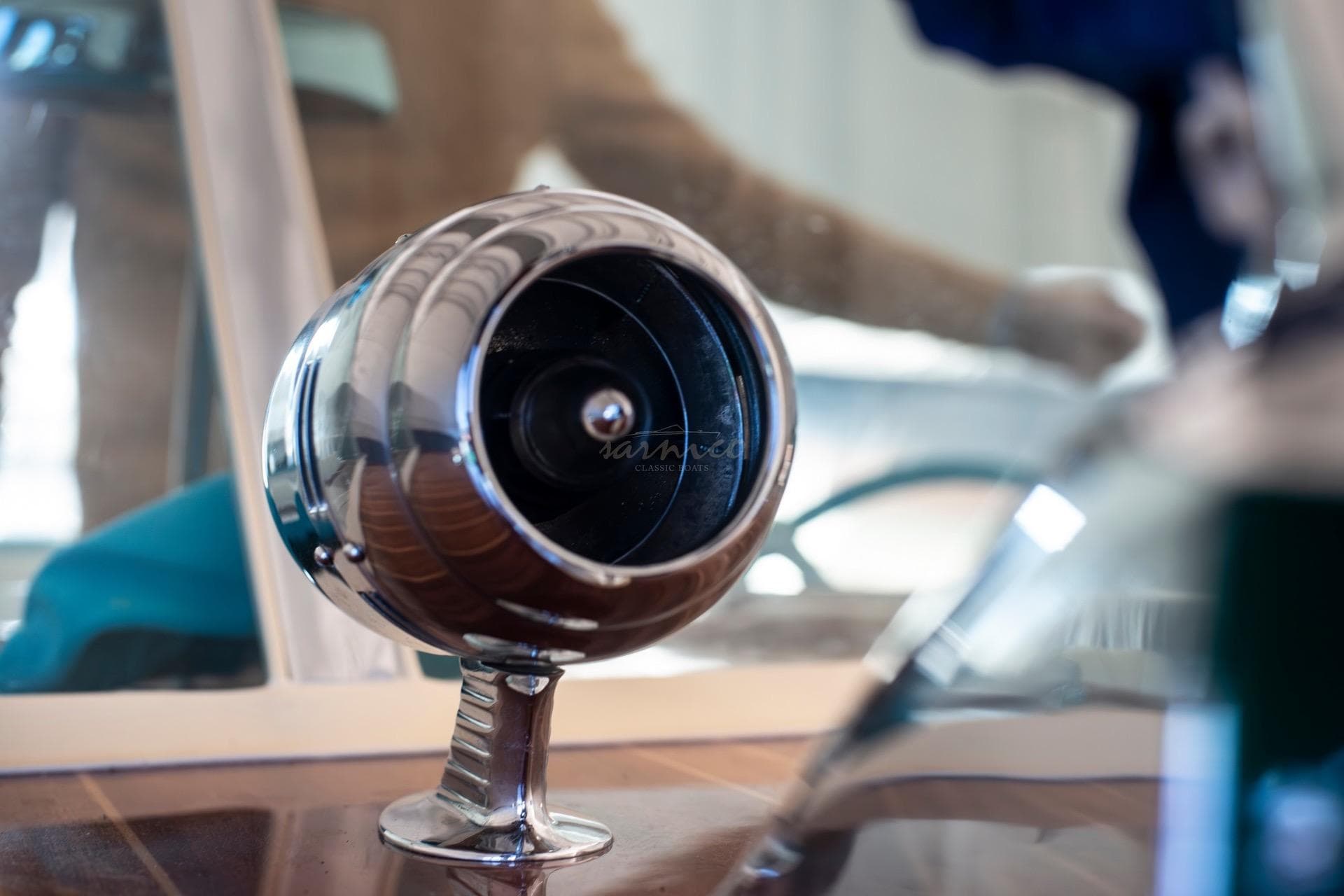 Close-up of a 1967 Riva Aquarama's chrome spotlight on a wooden dashboard.