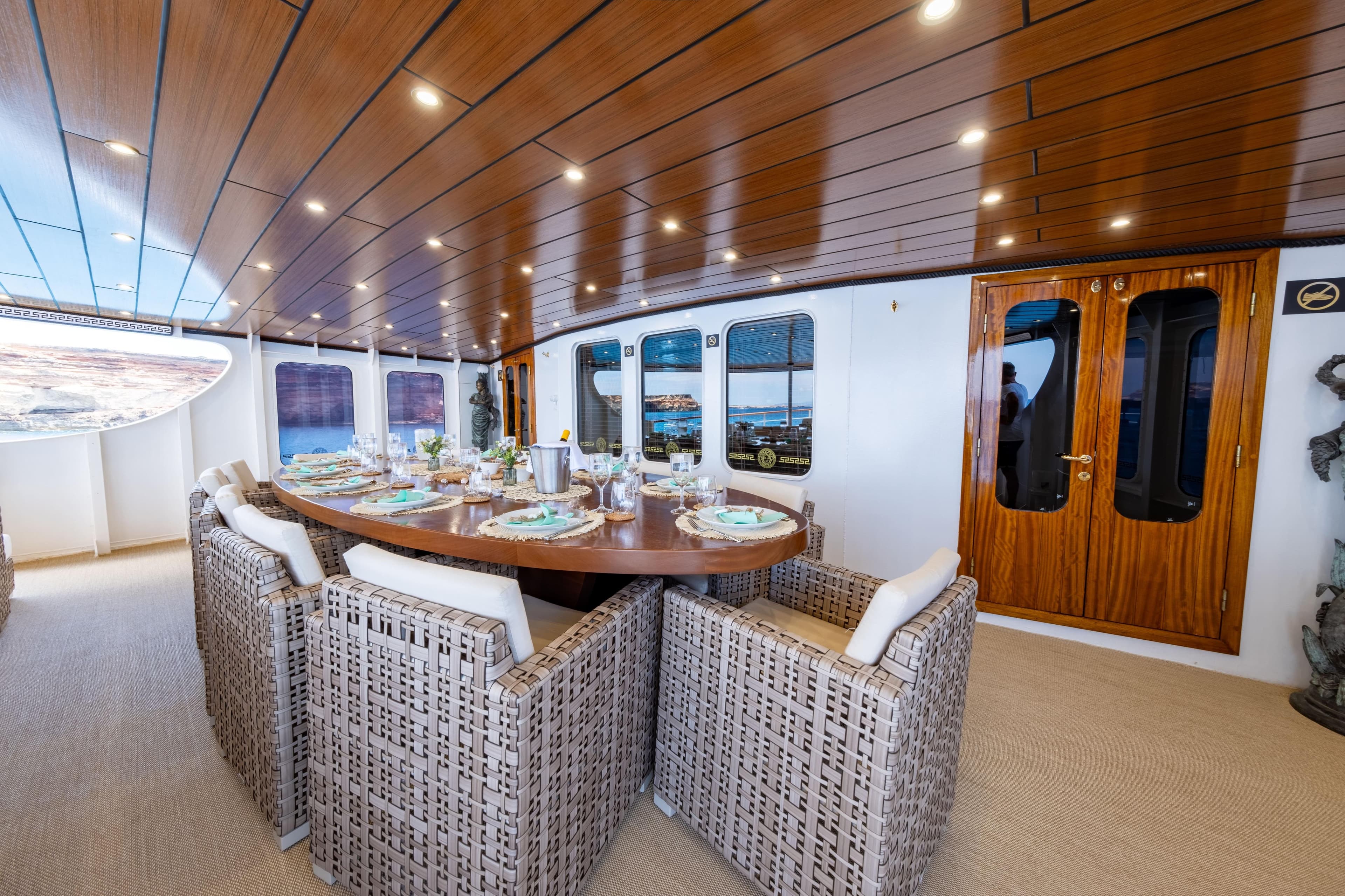 Luxurious yacht dining area with elegant table setting, wicker chairs, and wooden ceiling, 1954 Jadranska Linjska Plovidba.