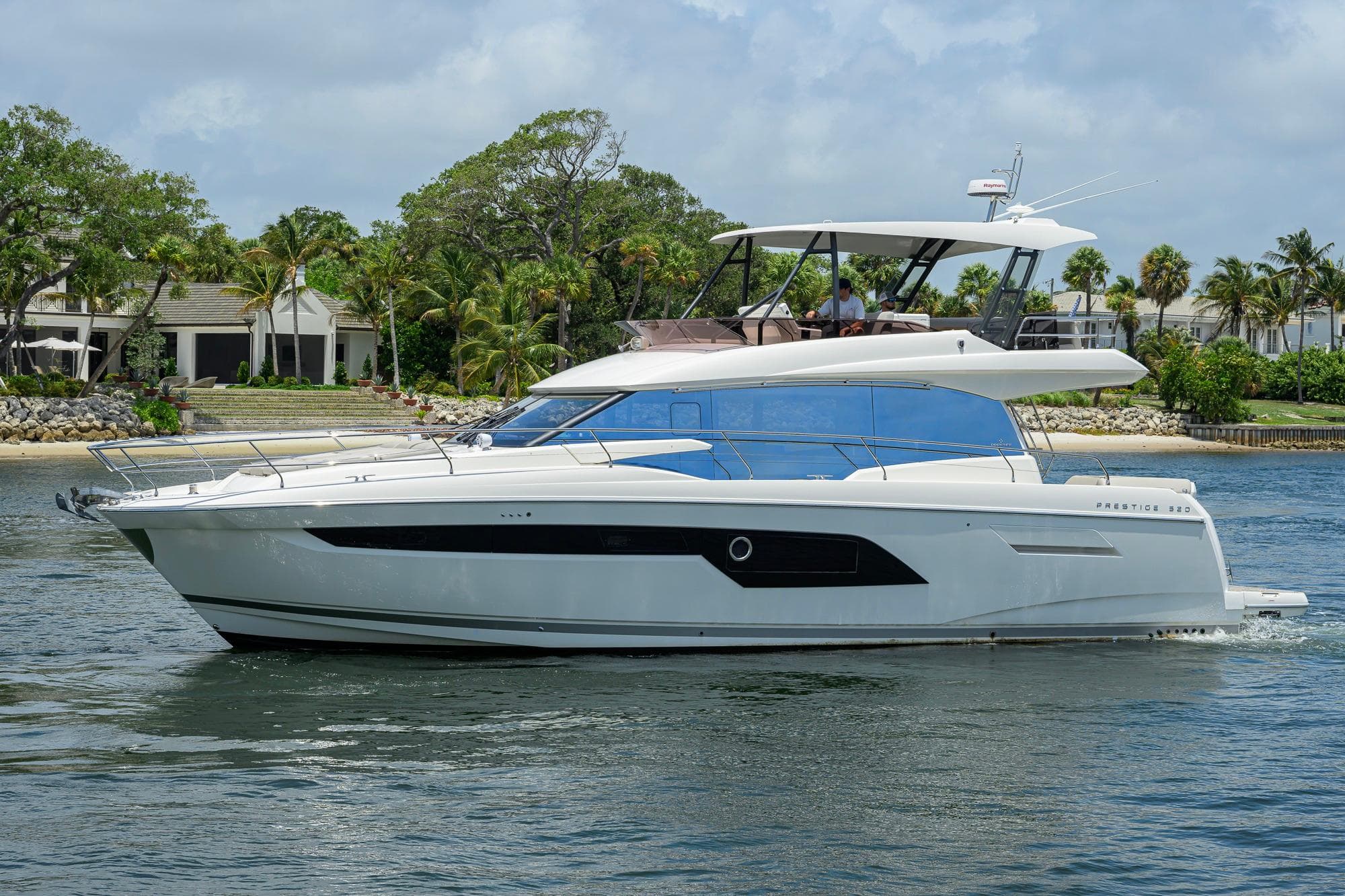 Luxury 2021 Prestige 520 yacht cruising near a tropical shoreline with lush greenery.