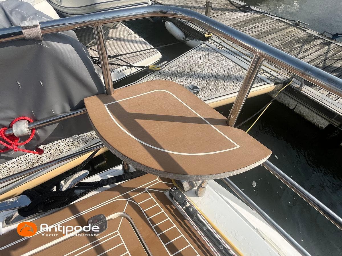 Deck of 2010 Amel 64 yacht with wooden table and railing at marina.