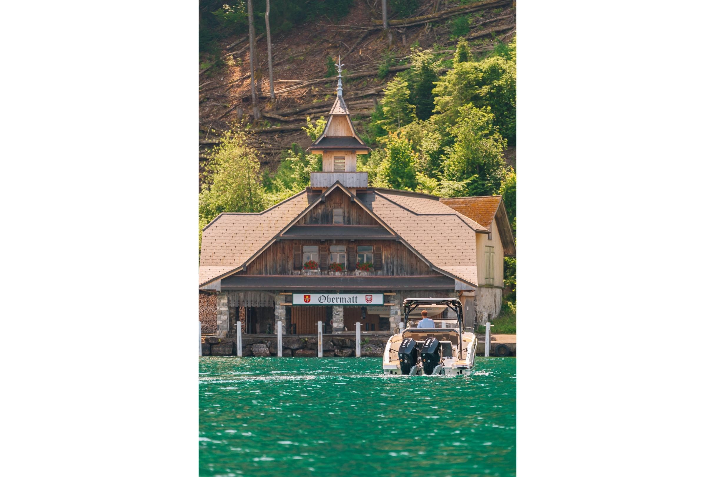 Boat on lake near rustic building, surrounded by lush greenery.