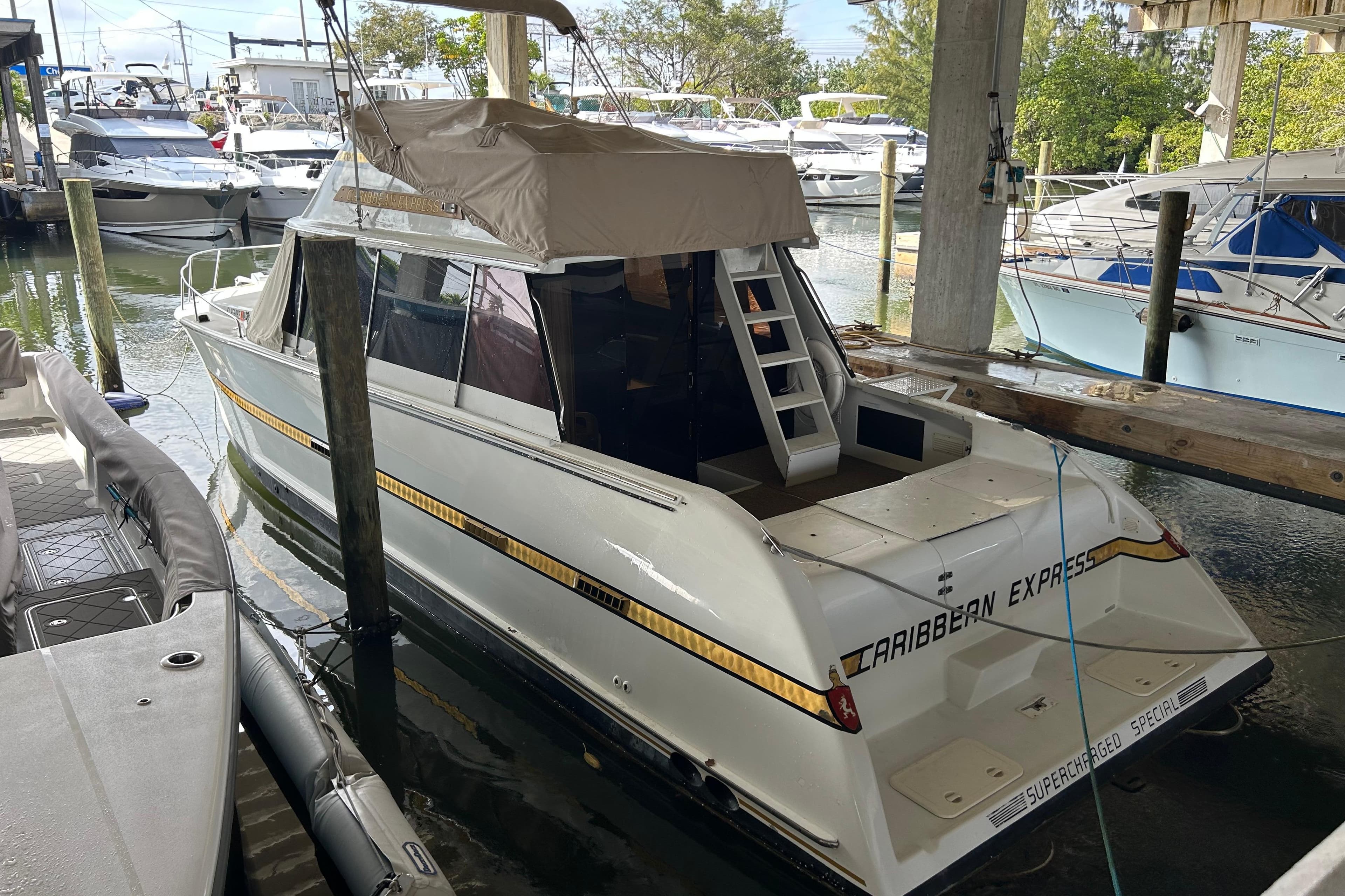 1984 Custom 38 boat "Caribbean Express" docked in marina, covered deck, surrounded by other boats.