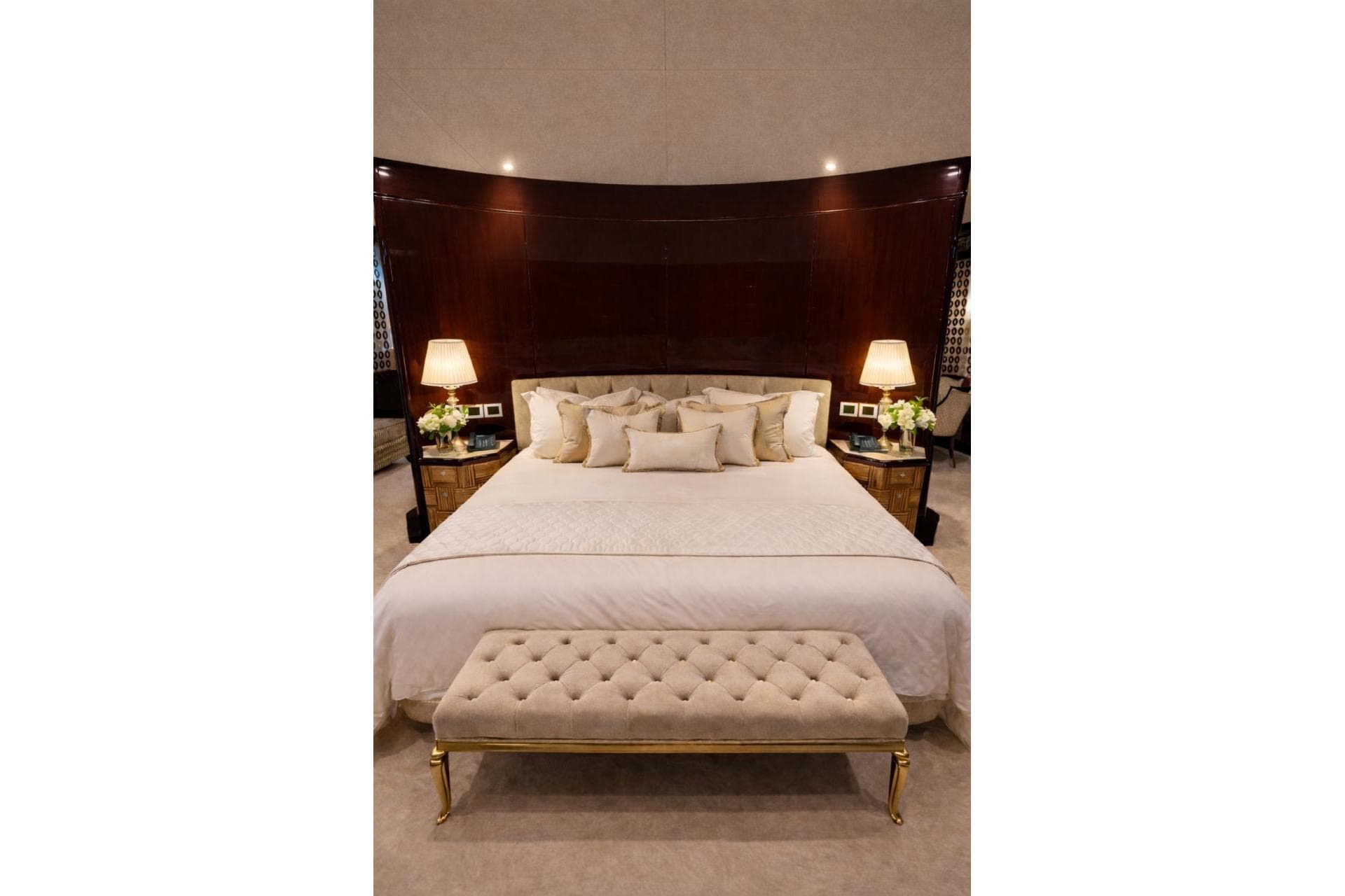 Luxurious bedroom with elegant decor, featuring a plush bed, lamps, and a tufted bench. Riviera 2010.