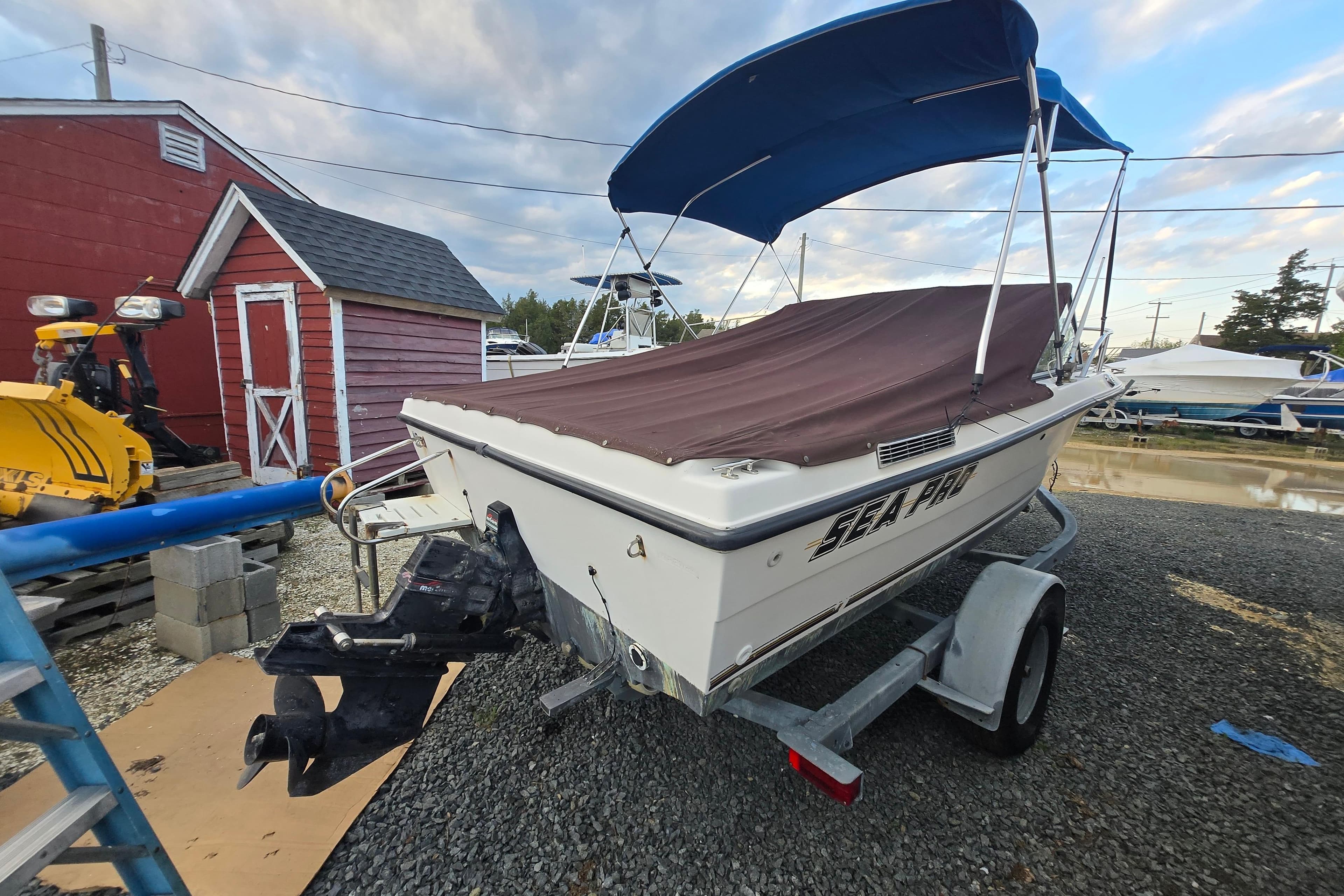 1994 Sea Pro 190 Dual Console boat on trailer, covered, with blue canopy, near red shed.