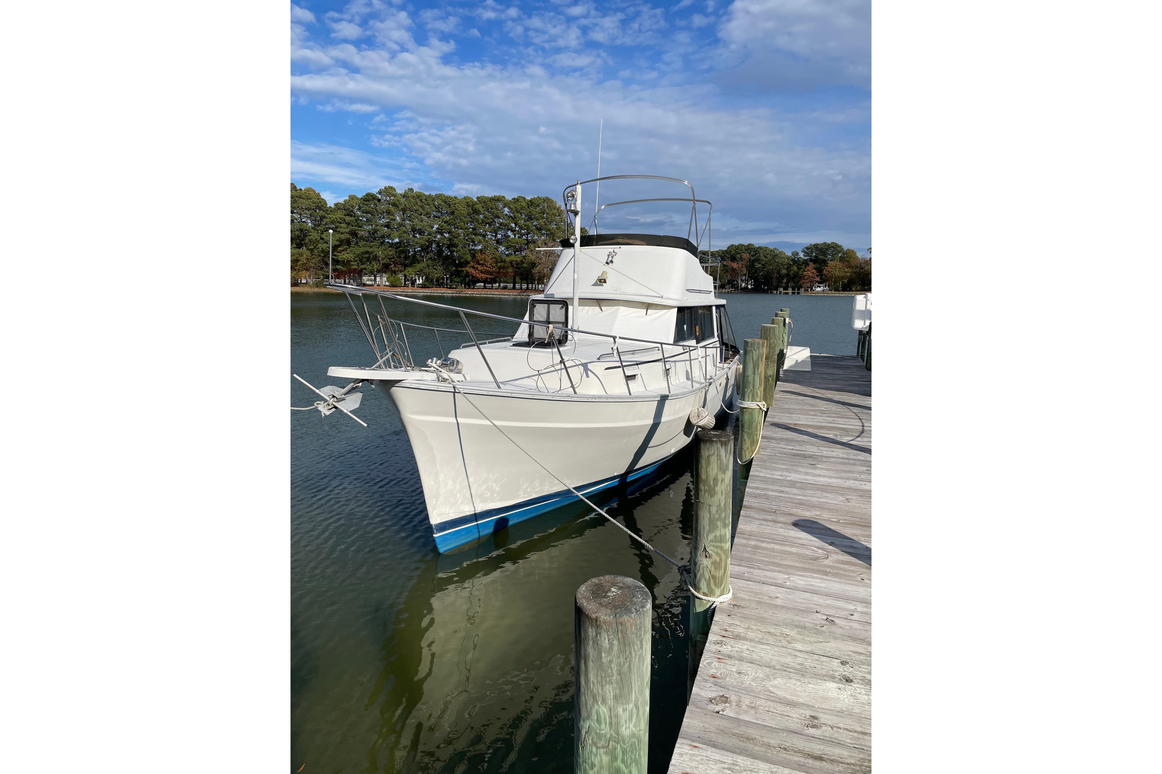 1982 Mainship 34 MK 1 yacht docked by a wooden pier under a blue sky.
