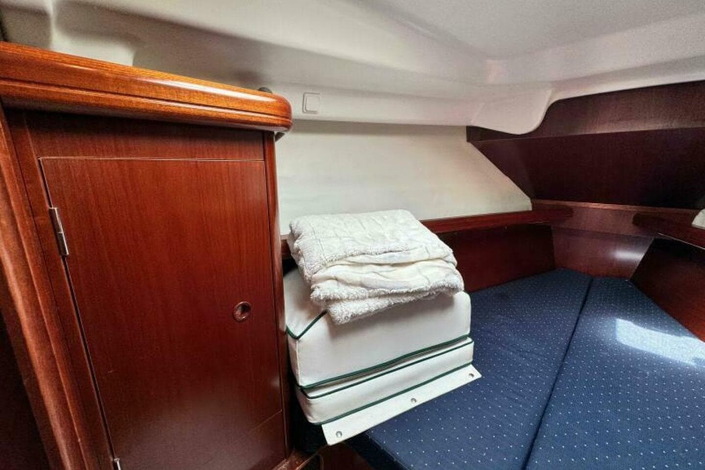 Interior cabin of 2004 Beneteau 323 sailboat with wooden cabinetry and cozy bedding.