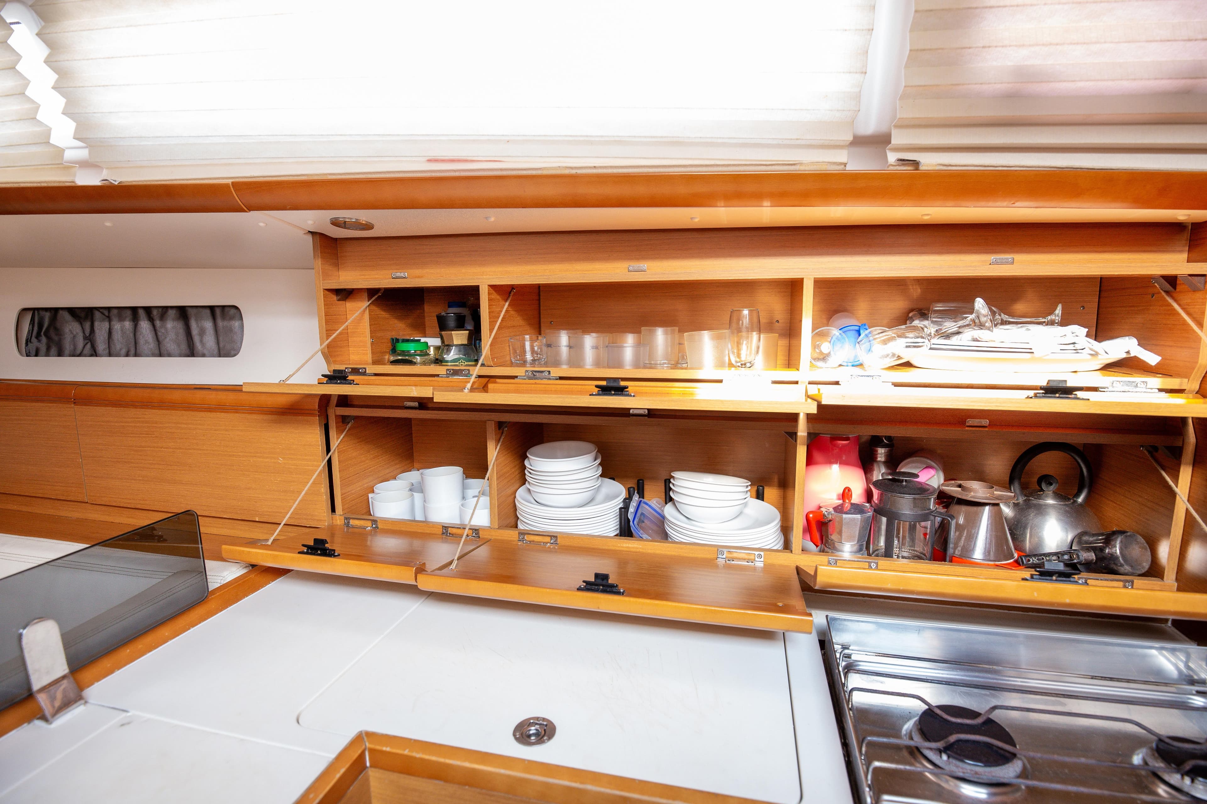 Interior of 2013 Jeanneau Sun Odyssey 439 yacht kitchen with open cabinets and kitchenware.