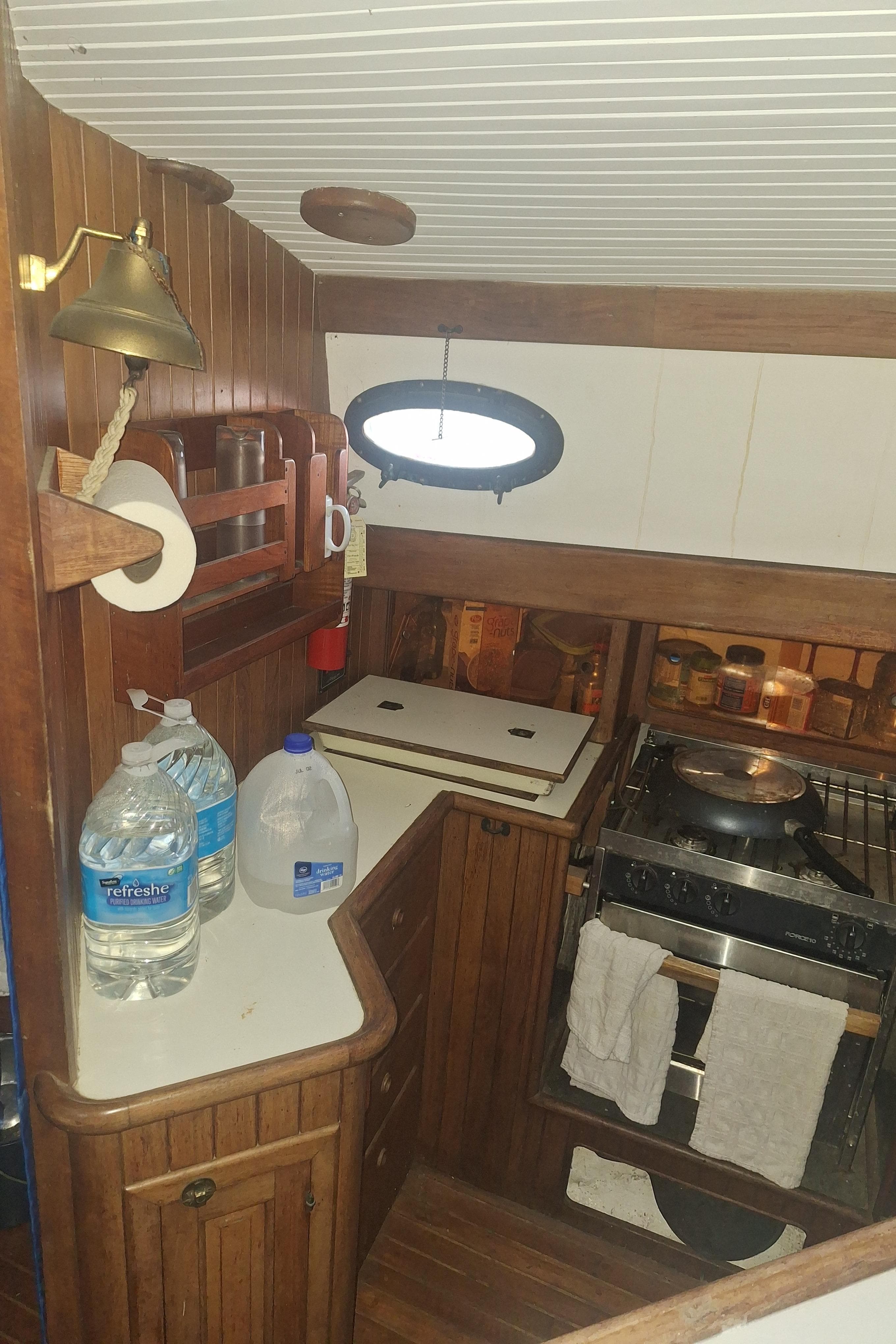 1977 Hans Christian 38 yacht galley with wood finish, stove, and water bottles.