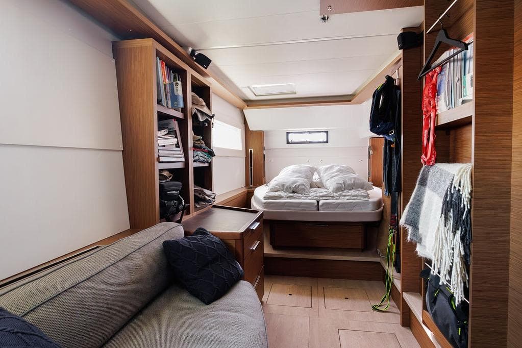 Interior of 2021 Lagoon 46 yacht cabin with bed, sofa, and wooden storage shelves.
