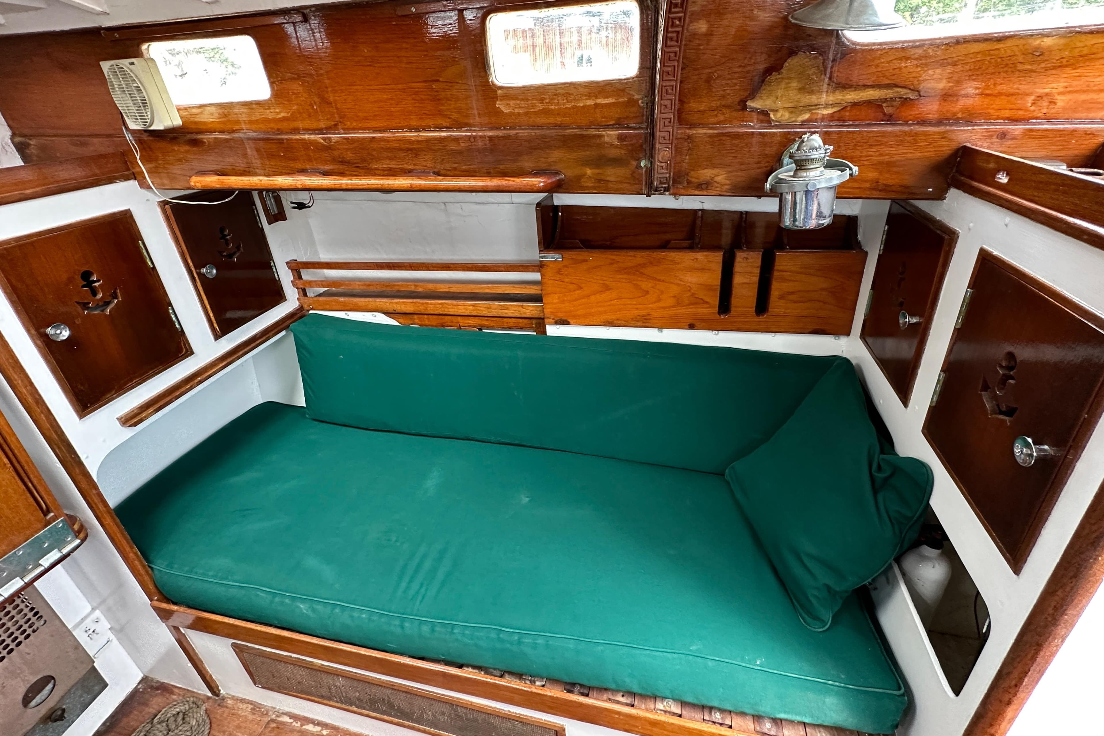 1964 Cheoy Lee Lion Class Sloop interior with green cushioned seating and wooden cabinetry.