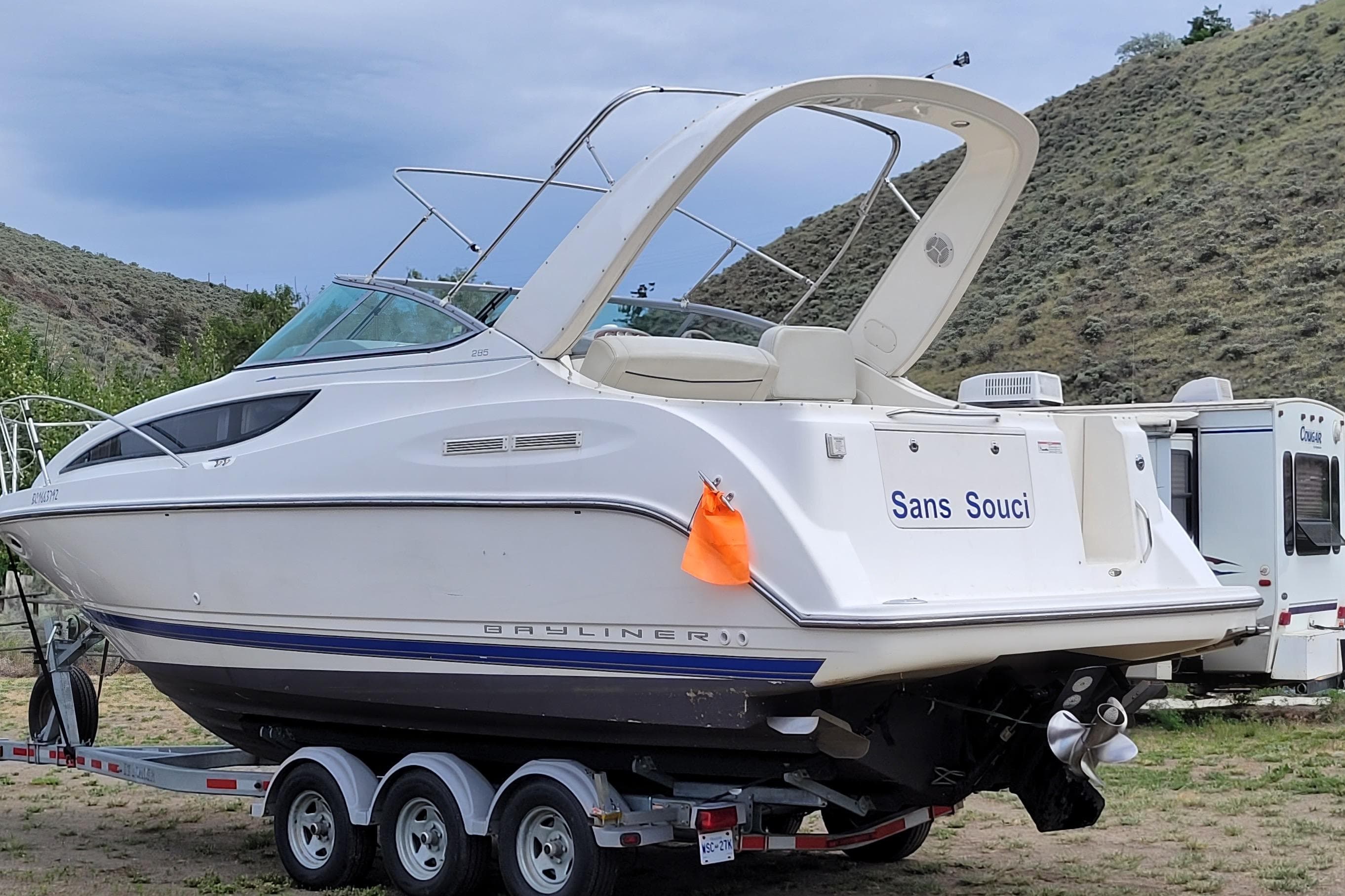2007 Bayliner 285 boat on trailer, named "Sans Souci," parked near hills and RV.