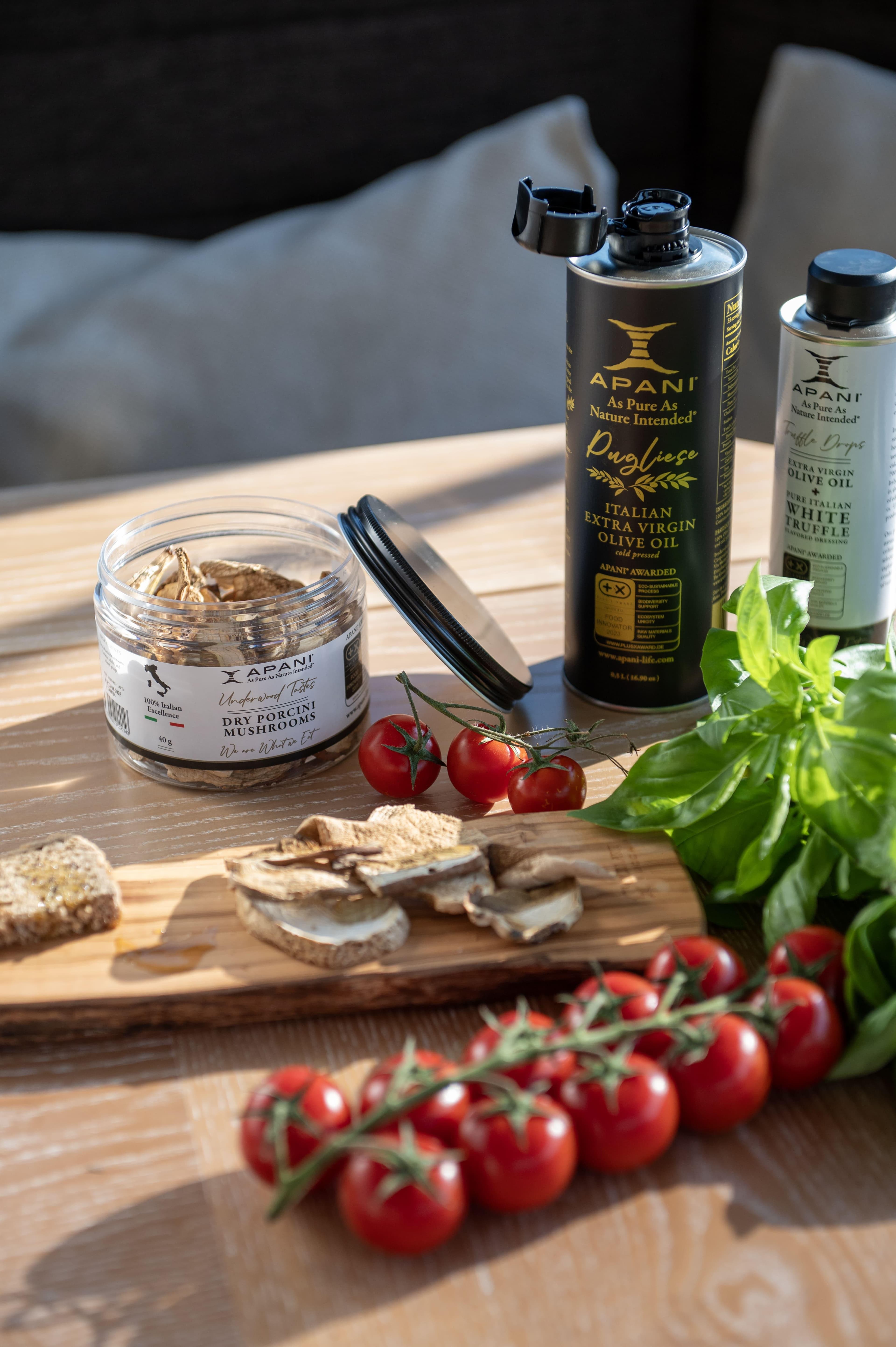 Gourmet ingredients on a wooden board: cherry tomatoes, basil, dried mushrooms, and olive oil.