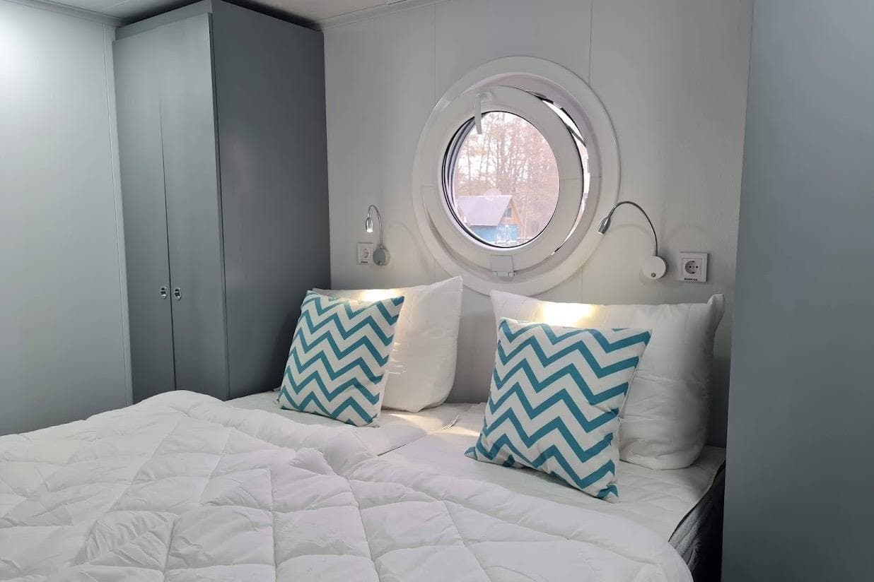 Cozy bedroom with round window, chevron pillows, and modern lighting in Woma D13, 2022 model.