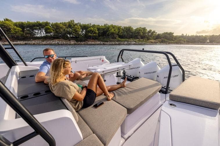 Couple relaxing on 2027 Axopar 45 Cross Top boat, enjoying scenic coastal view.