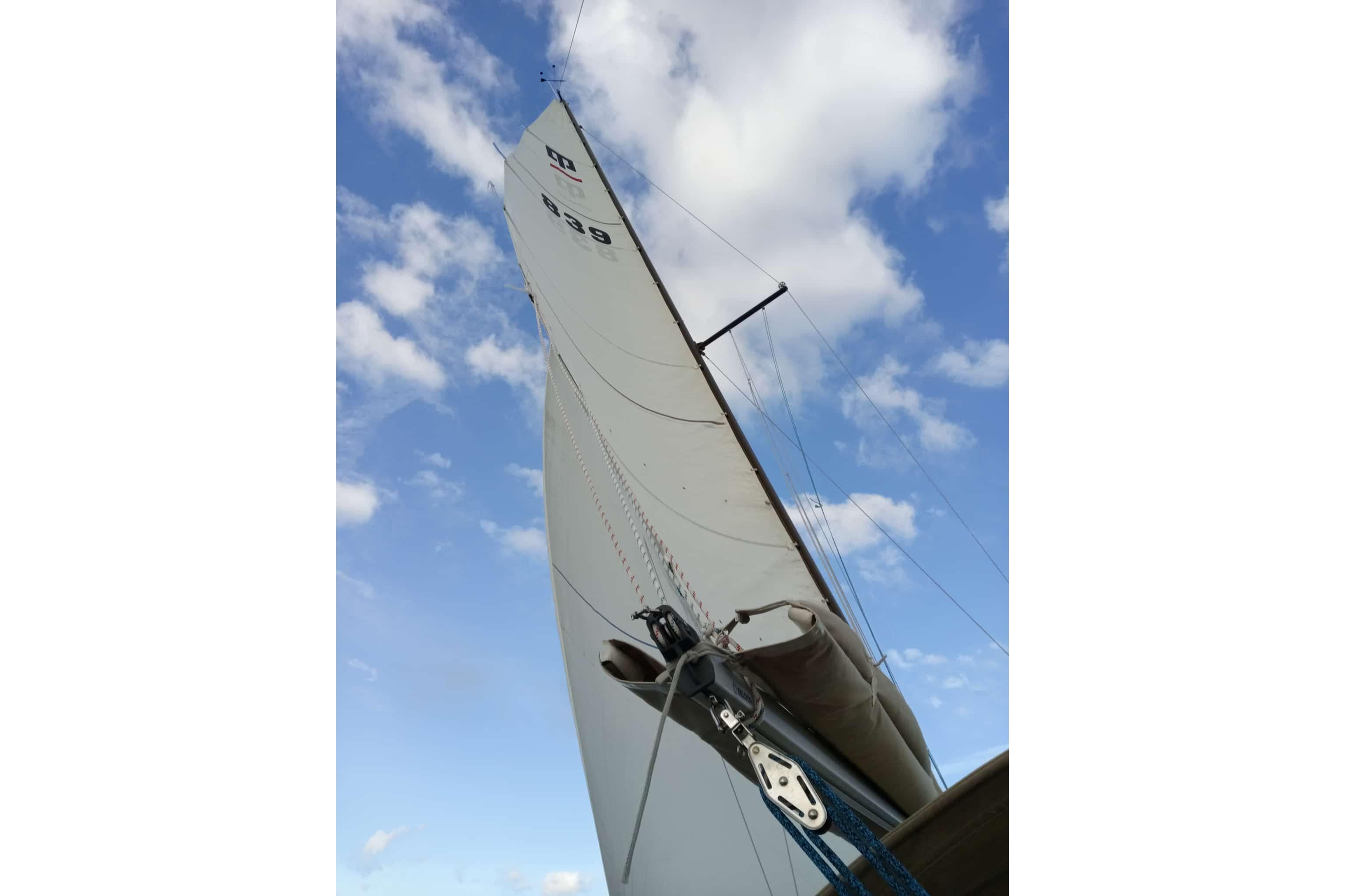 Sail of 1980 Dehler Optima 98 yacht against a blue sky with clouds.