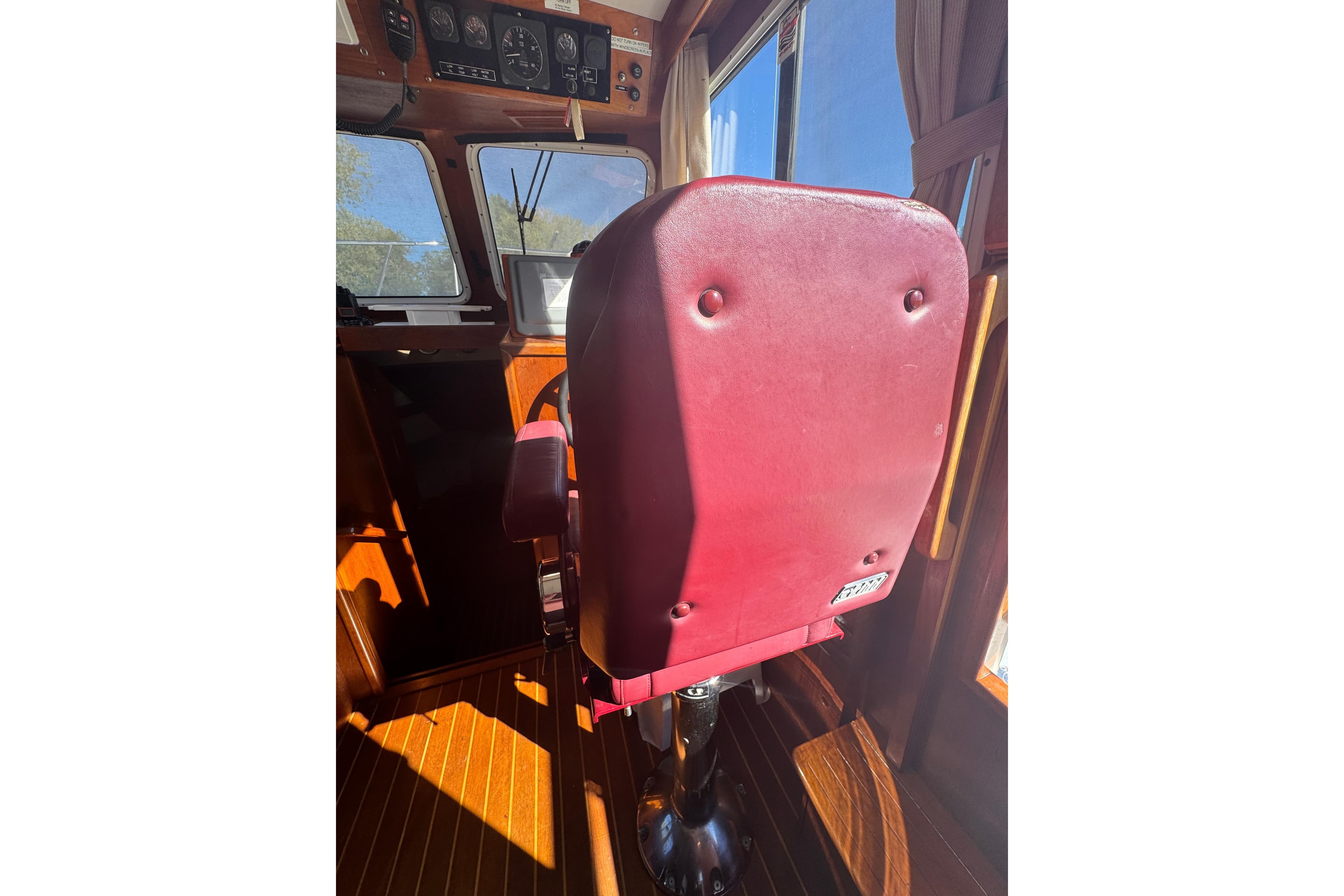 Captain's chair in 2001 Monk Trawler boat cockpit, featuring red upholstery and wooden interior.