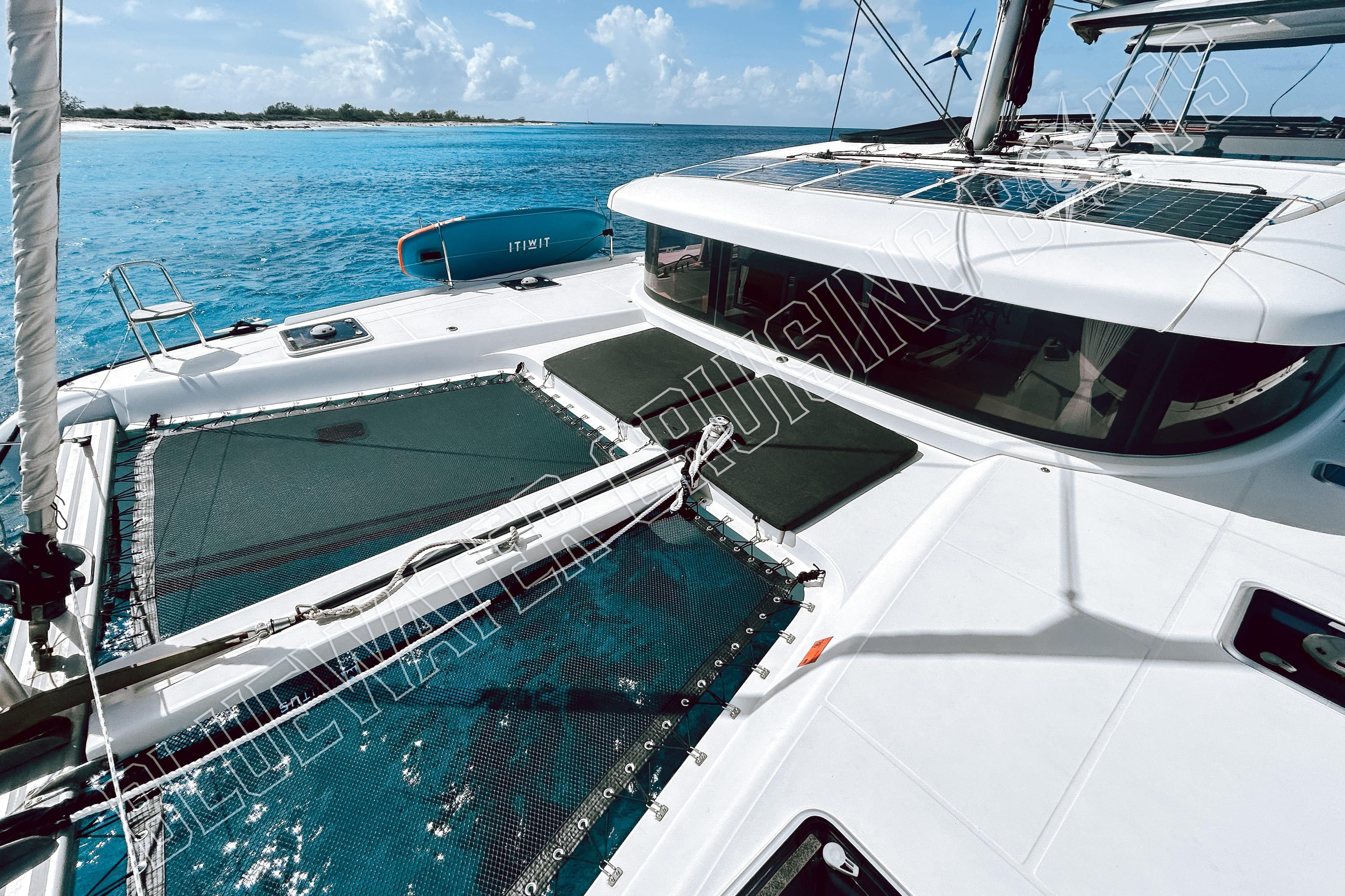 2018 Lagoon 42 catamaran on turquoise waters, featuring solar panels and netted deck.