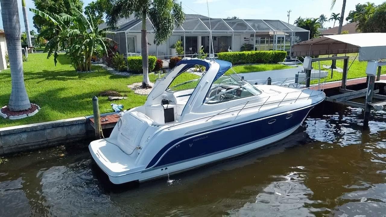 2003 Formula 37PC boat docked near a waterfront home.
