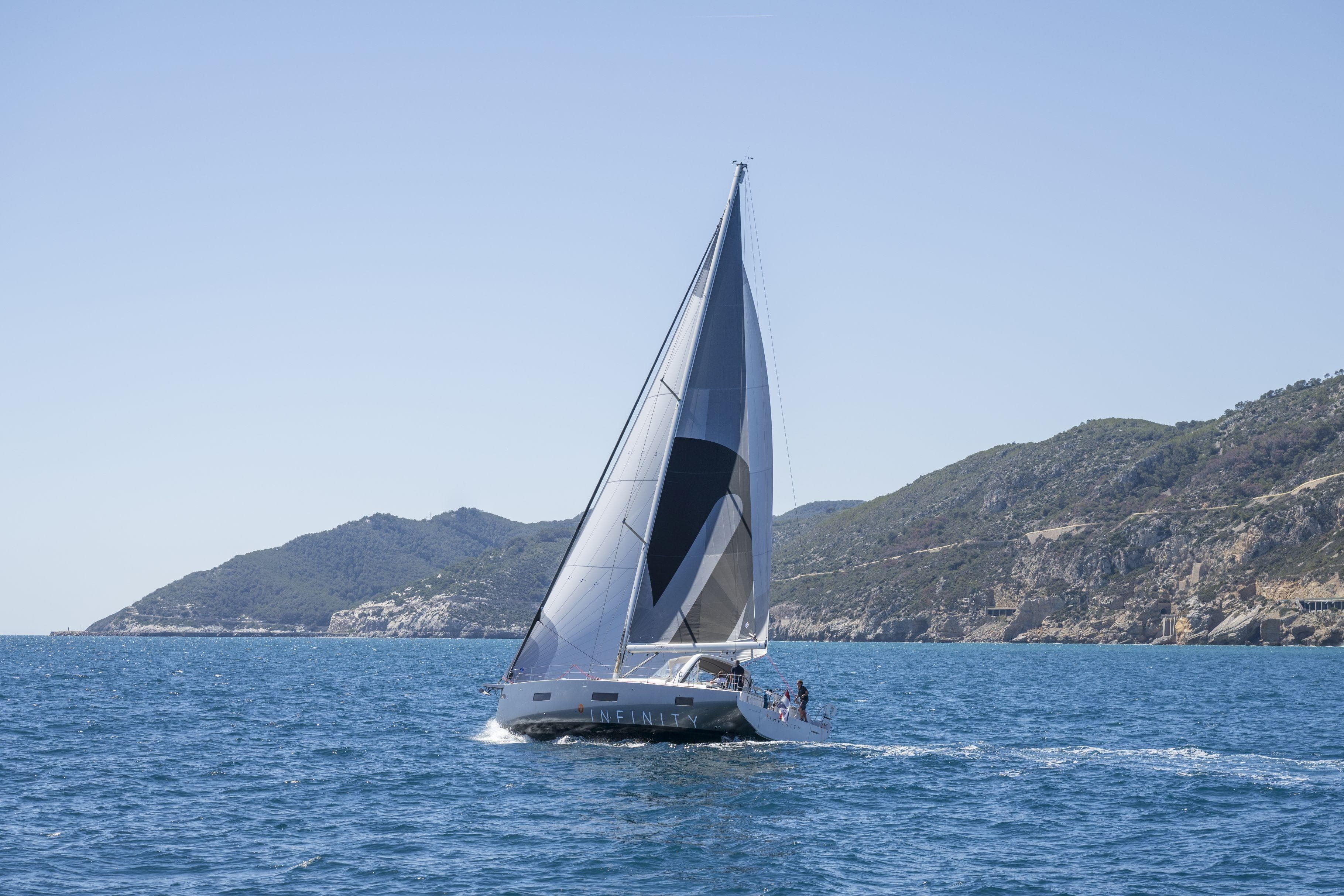 2023 Beneteau Oceanis Yacht 60 sailing near scenic coastal mountains.