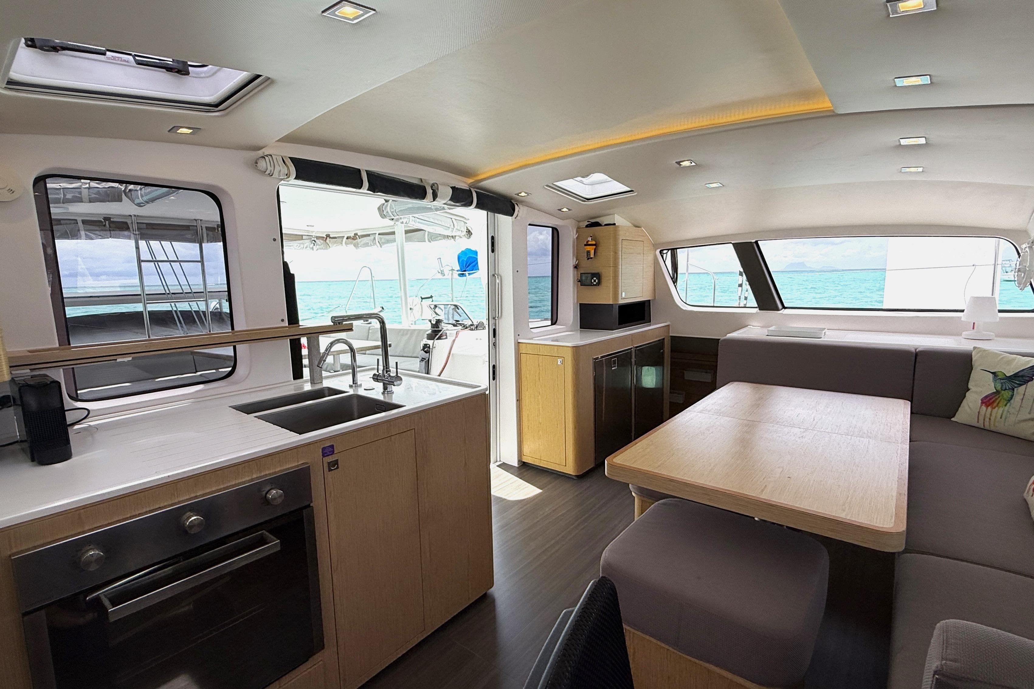 Modern interior of 2023 Outremer 51 catamaran featuring kitchen and dining area with ocean view.