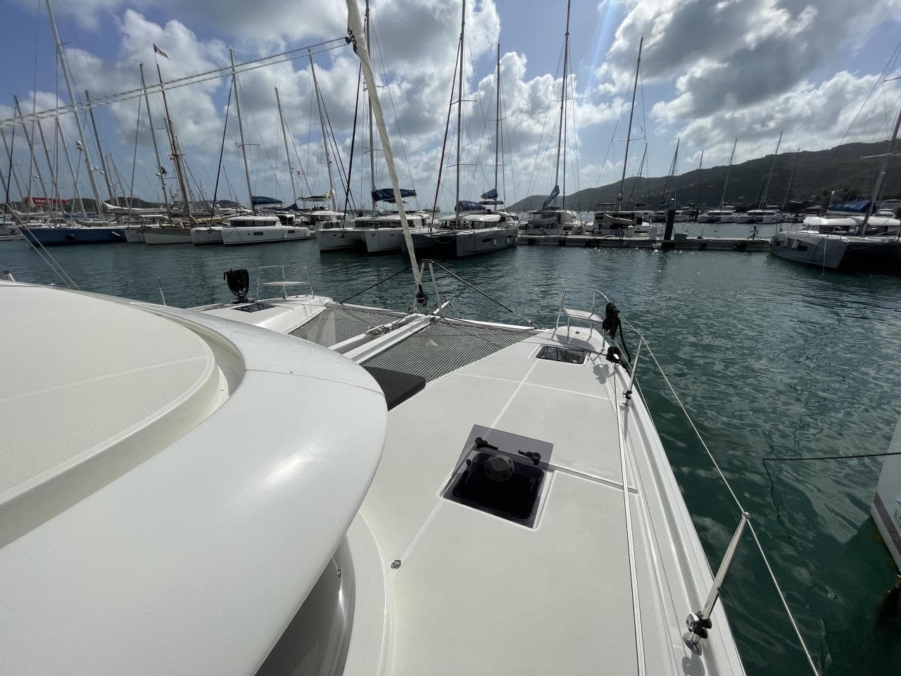2023 CNB Lagoon 46 catamaran docked in a marina, surrounded by sailboats under a cloudy sky.