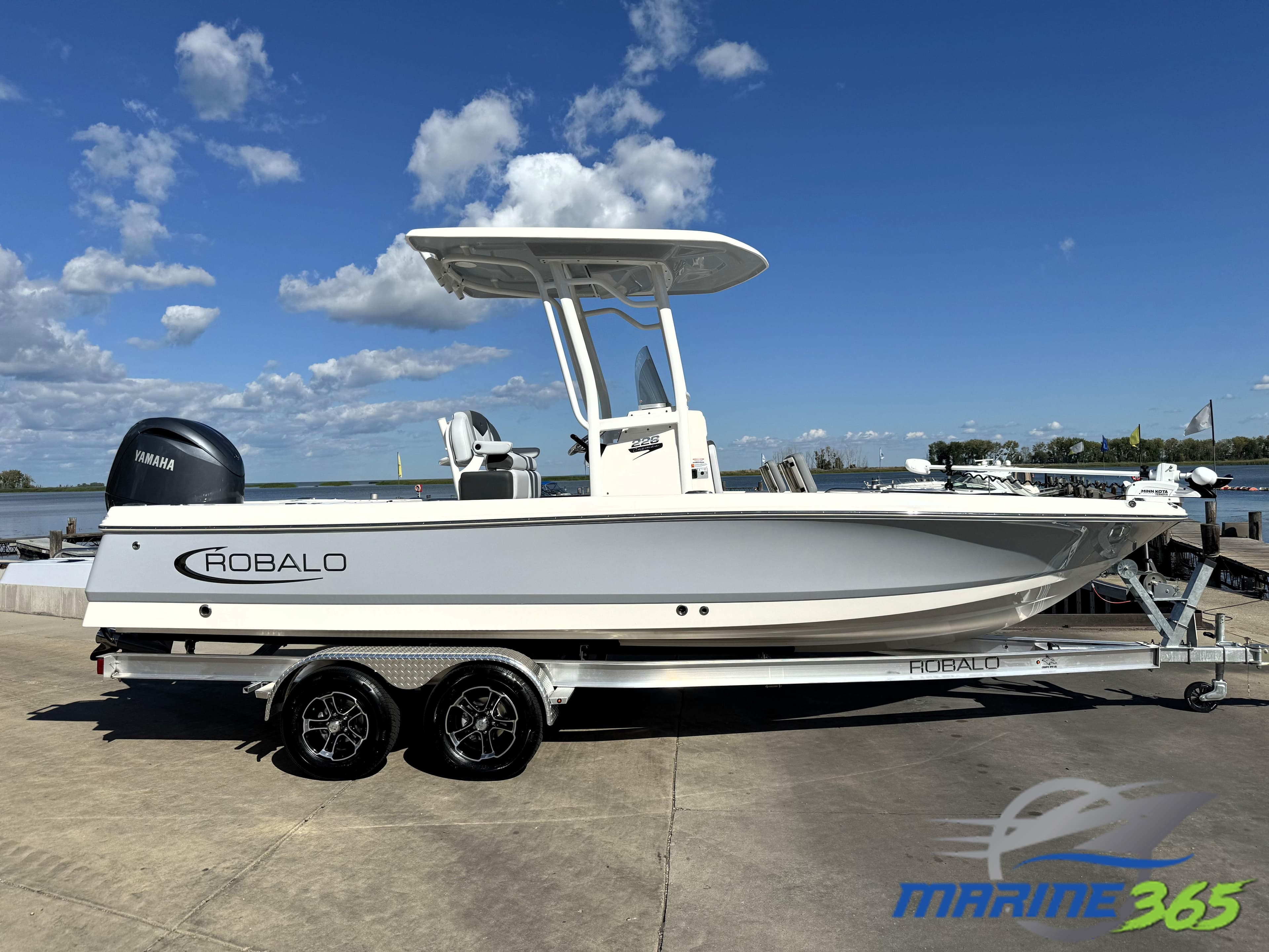 2025 Robalo 226 Cayman boat on trailer, parked by waterfront under blue sky.