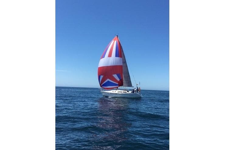 Sailboat Catalina 320 (1999) with colorful spinnaker on open sea under clear blue sky.