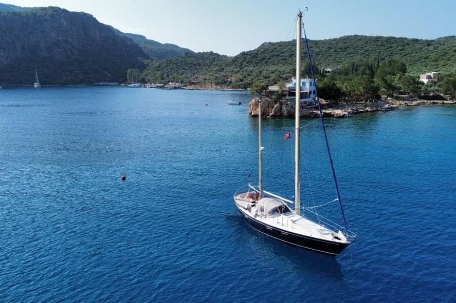 Sailboat Dufour Sortilege 41 (1972) anchored in scenic coastal bay with lush greenery.