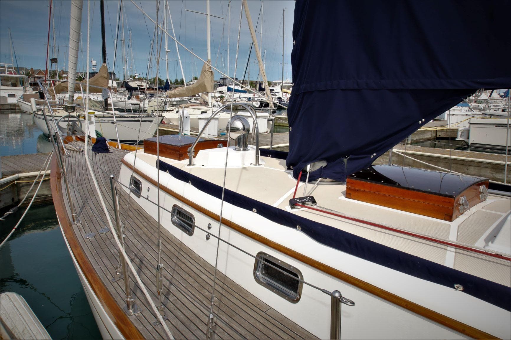 1986 Mason 33 sailboat docked in a marina, featuring wooden deck and blue sail cover.