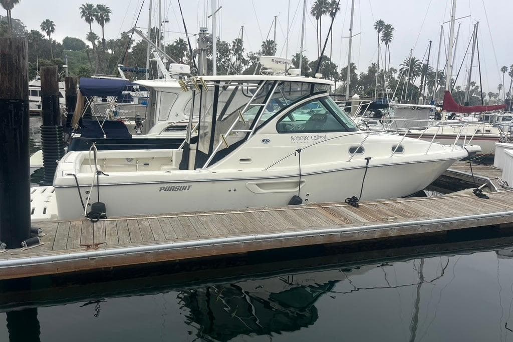 2005 Pursuit 3100 Offshore boat docked at a marina with palm trees in the background.