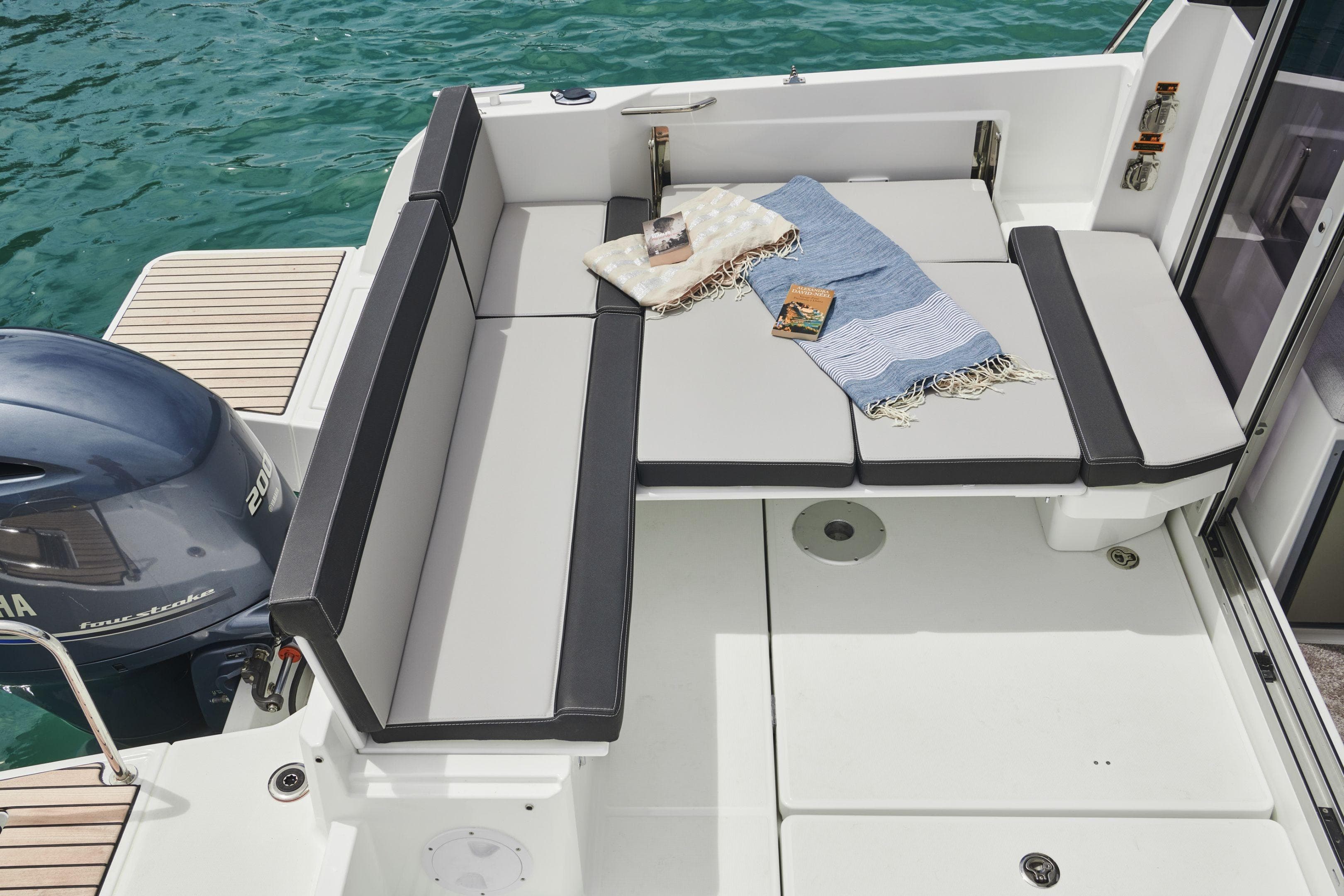 2026 Jeanneau NC 795 Series 2 boat deck with seating, blankets, and books by the water.