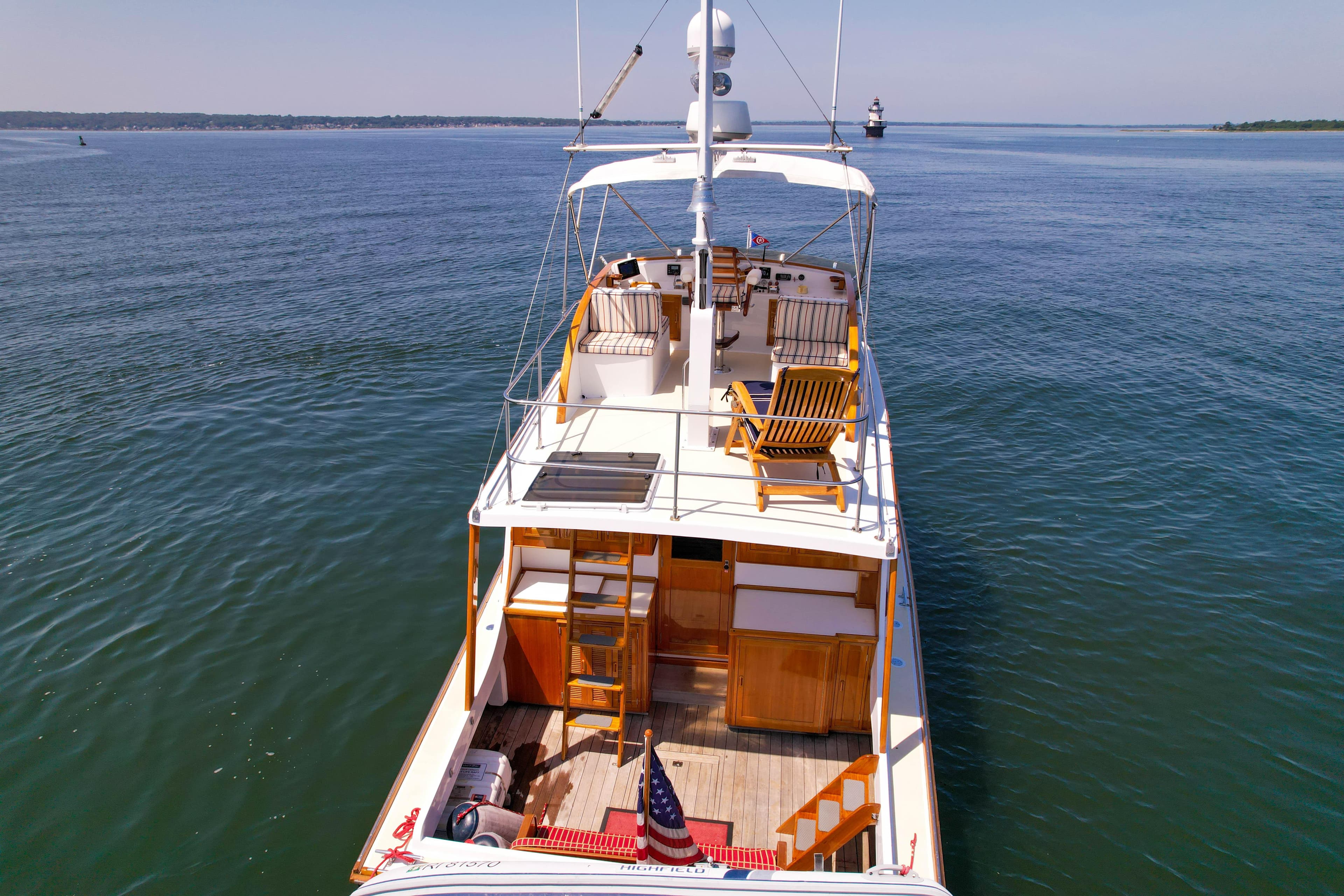 1984 Wilbur 38 yacht on calm water, featuring wooden deck chairs and American flag.