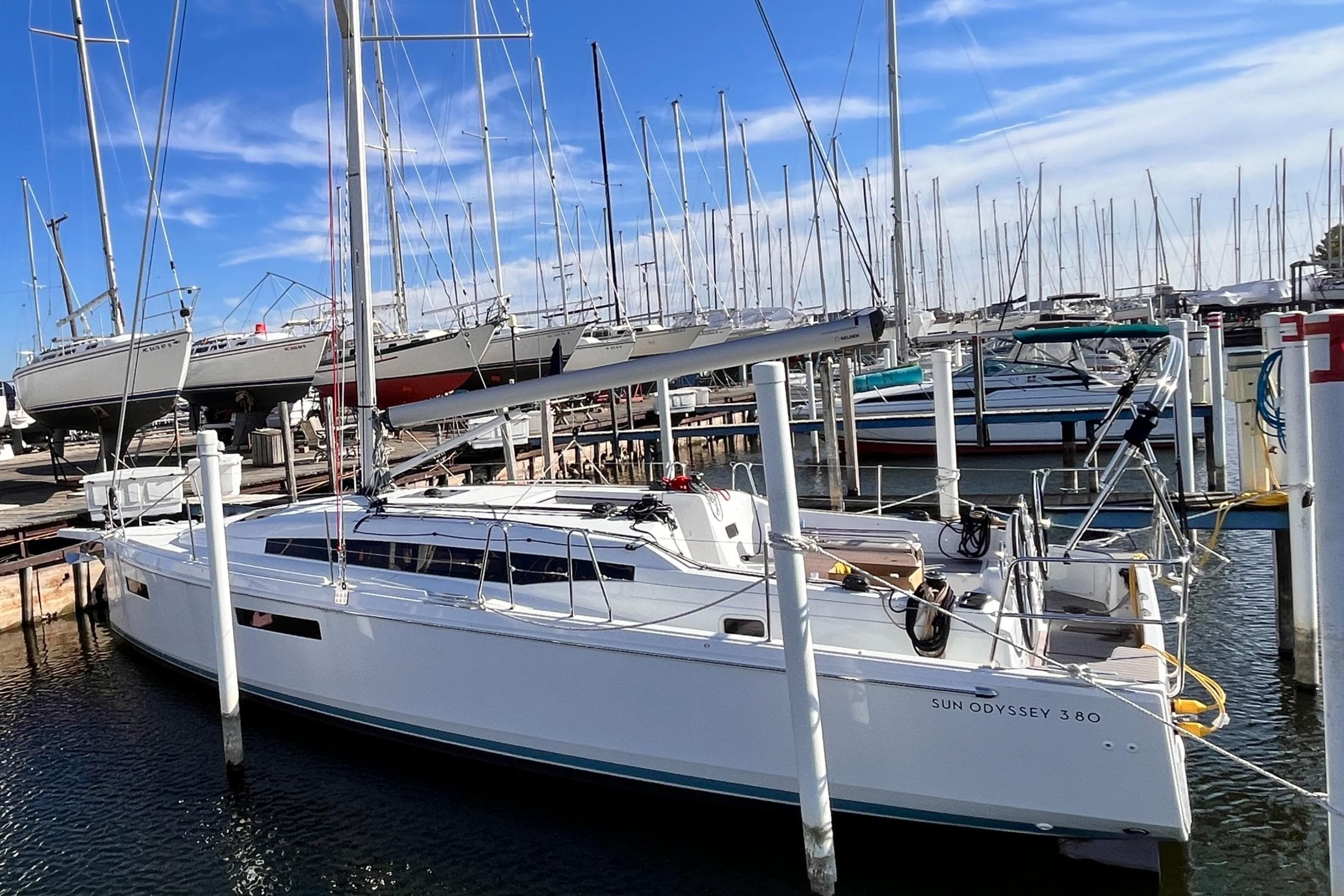 2024 Jeanneau 380 sailboat docked in marina, clear blue sky, multiple sailboats in background.