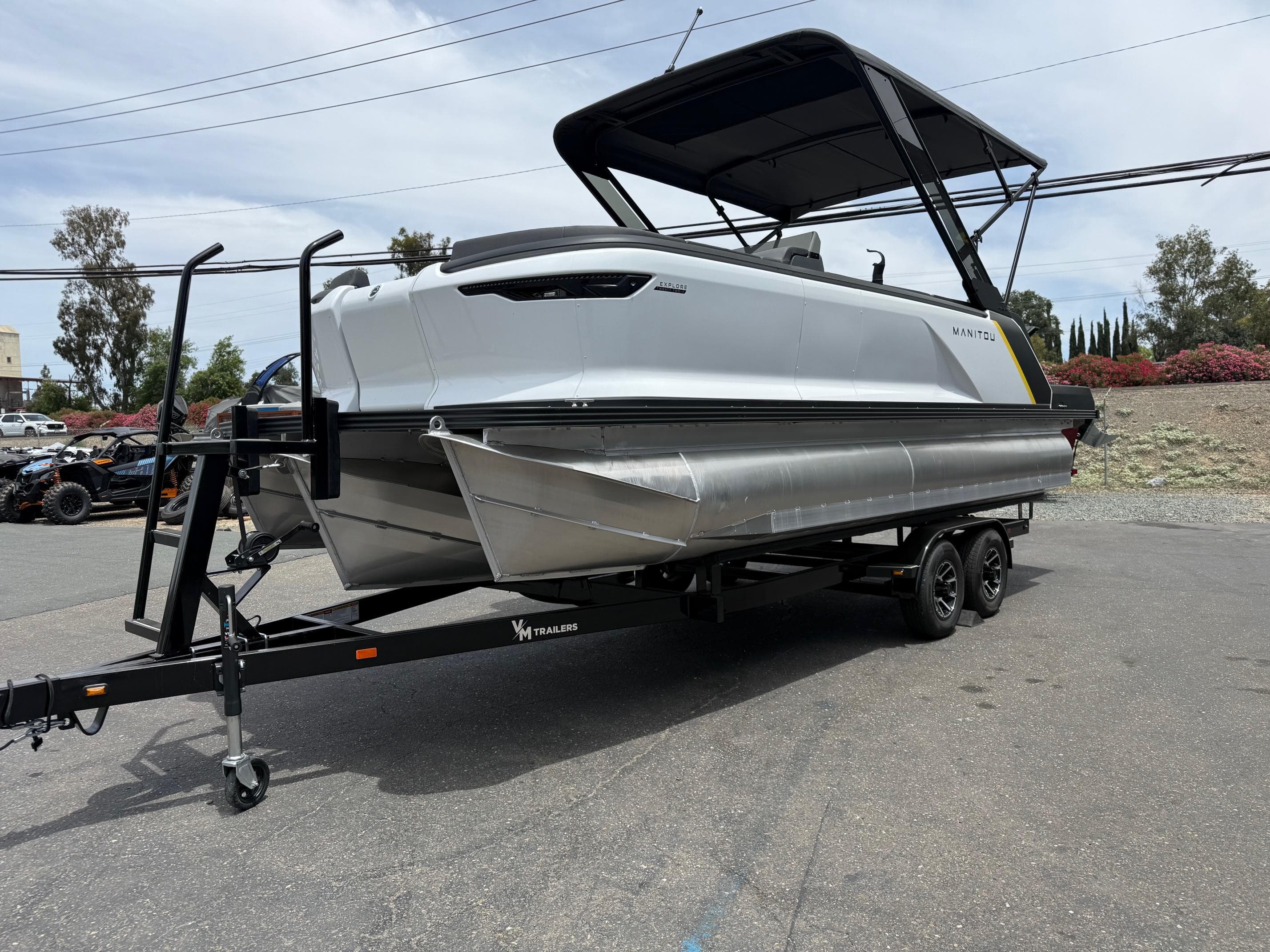 2025 Manitou Explore pontoon boat on trailer, parked outdoors.