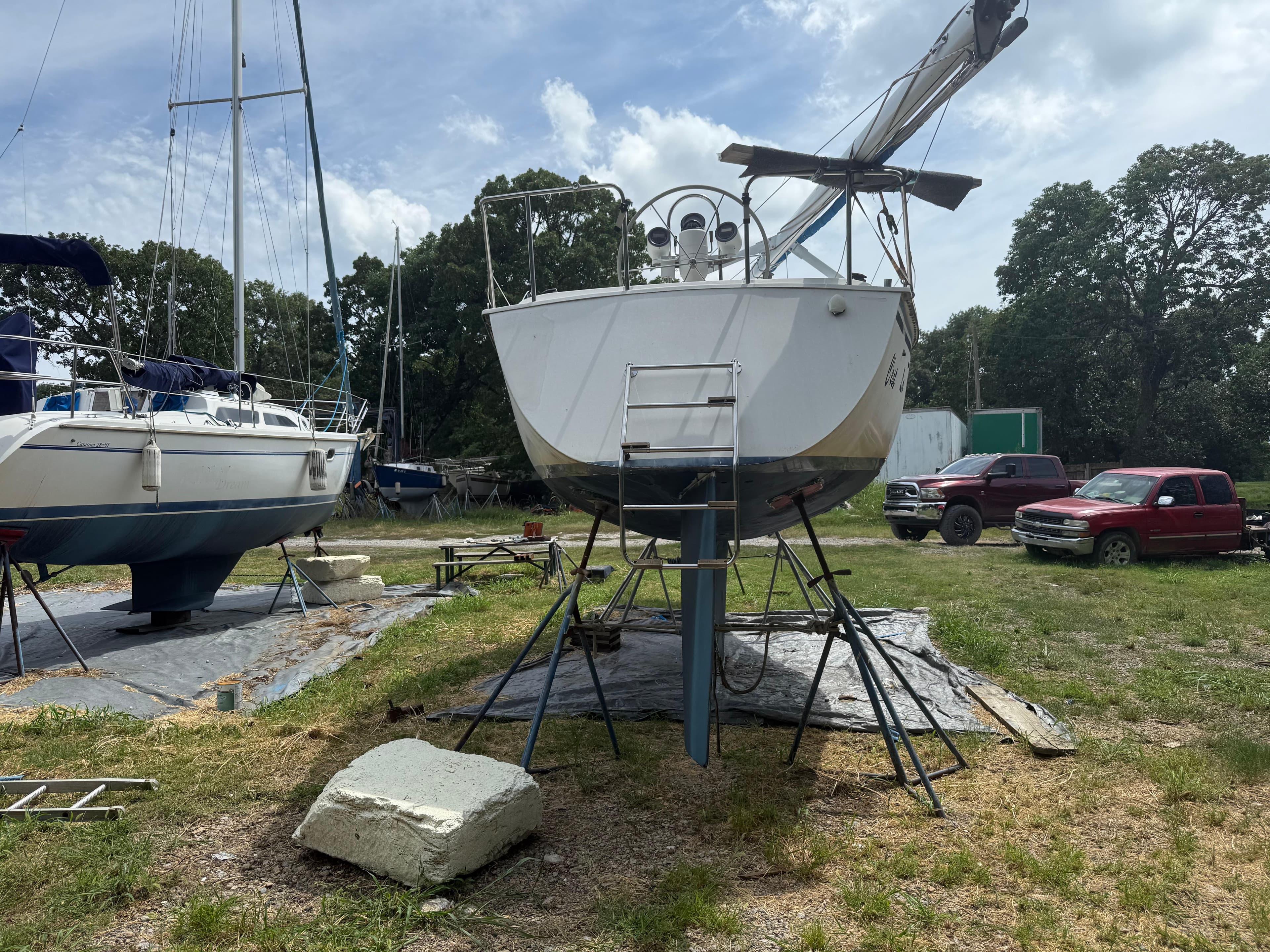 1986 Hunter 28.5 sailboat on stands, surrounded by grass and parked vehicles.