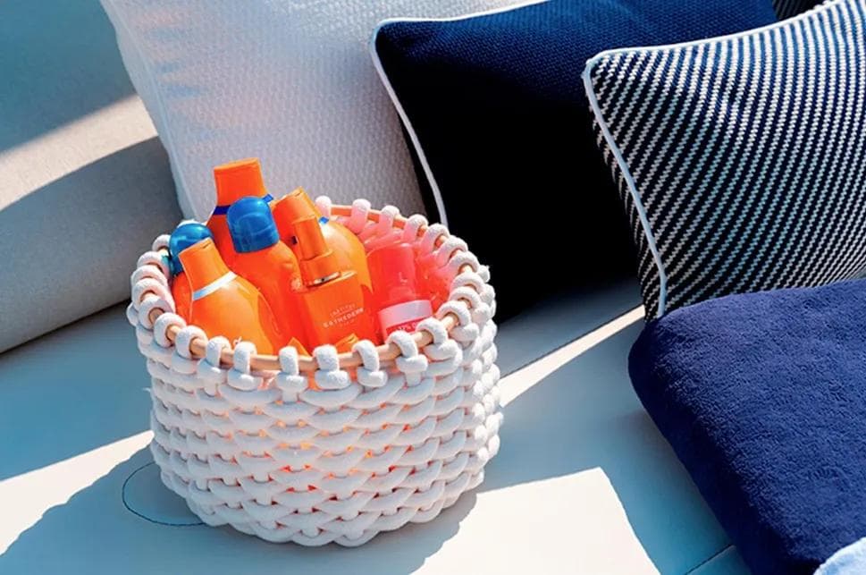 Basket of sunscreen bottles on Invictus TT460 yacht, 2023, with blue and white cushions.