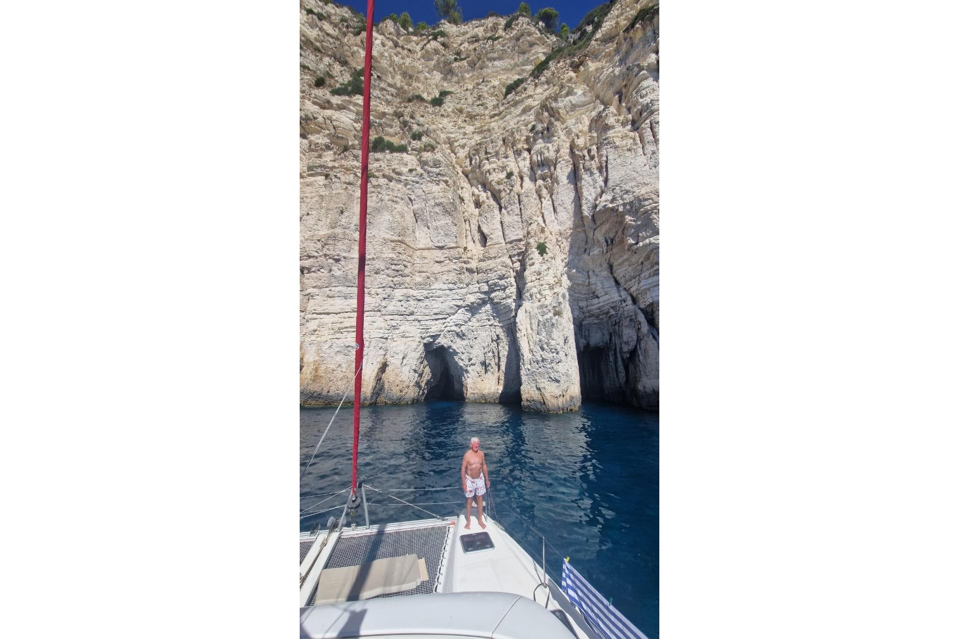 Man on Lagoon 42 catamaran near rocky cliffs, clear blue water, sunny day.