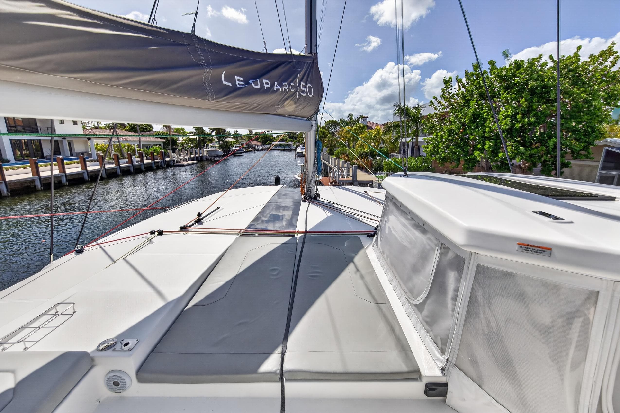 Leopard 50 catamaran, 2022 model, docked in a sunny canal with lush greenery.