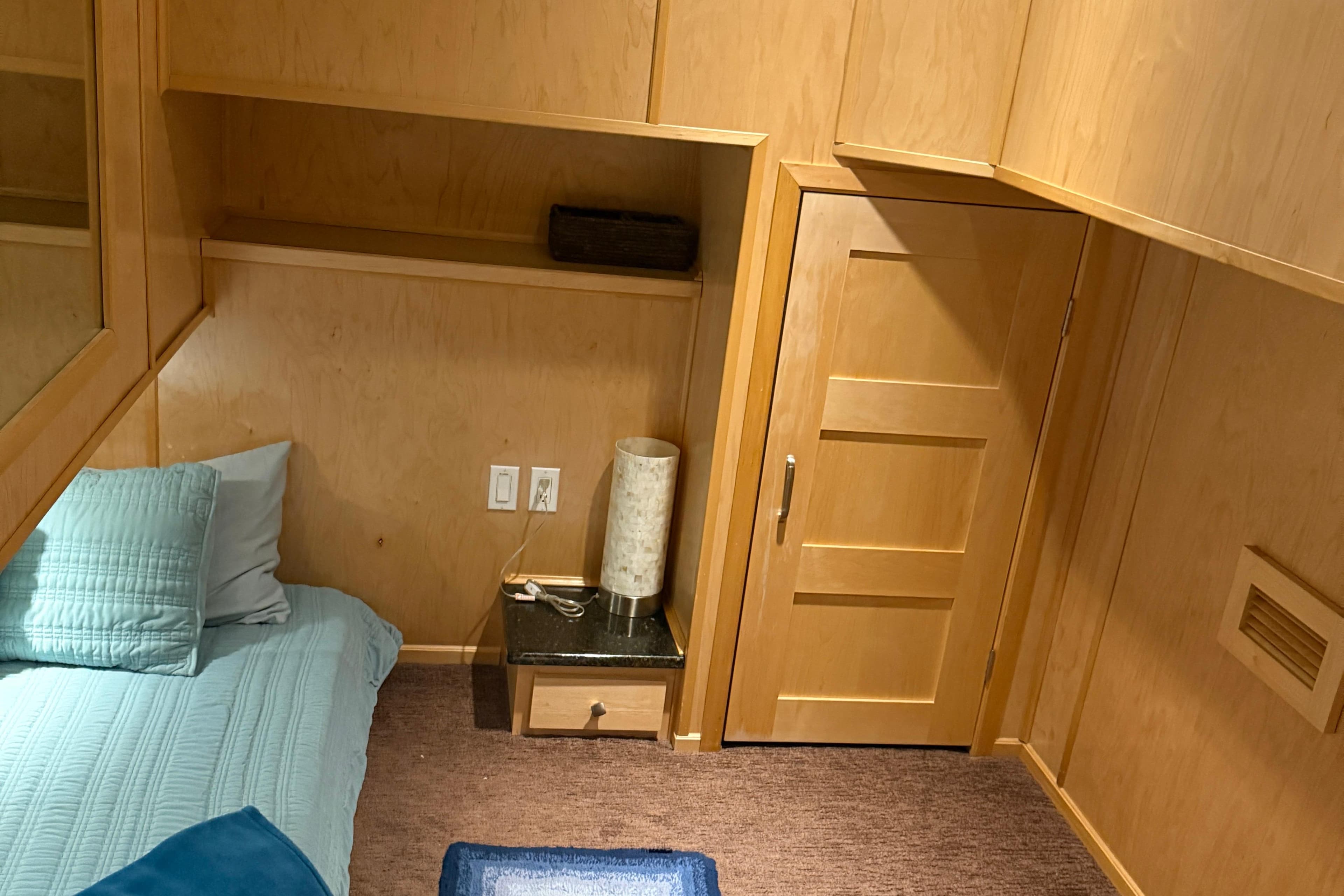 Cozy bedroom with wooden walls, blue bedding, and a small nightstand in STARDUST Oceans Share #2, 2015.