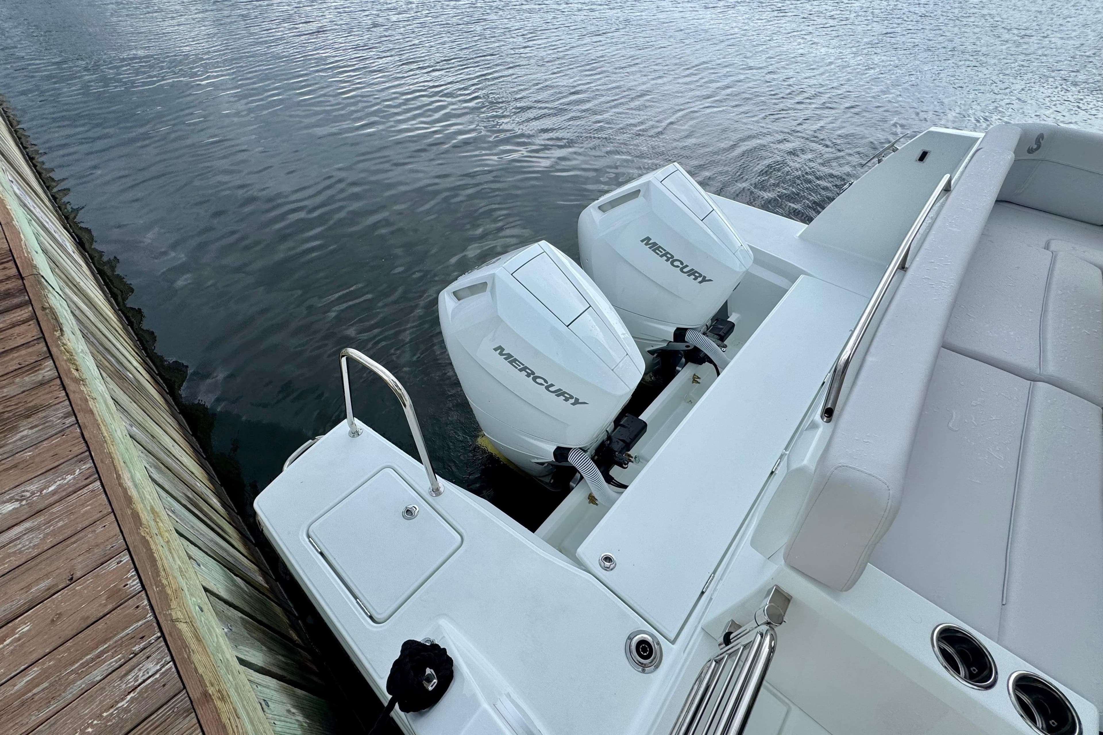 2026 Beneteau Antares 12 with dual Mercury outboard engines docked by wooden pier.