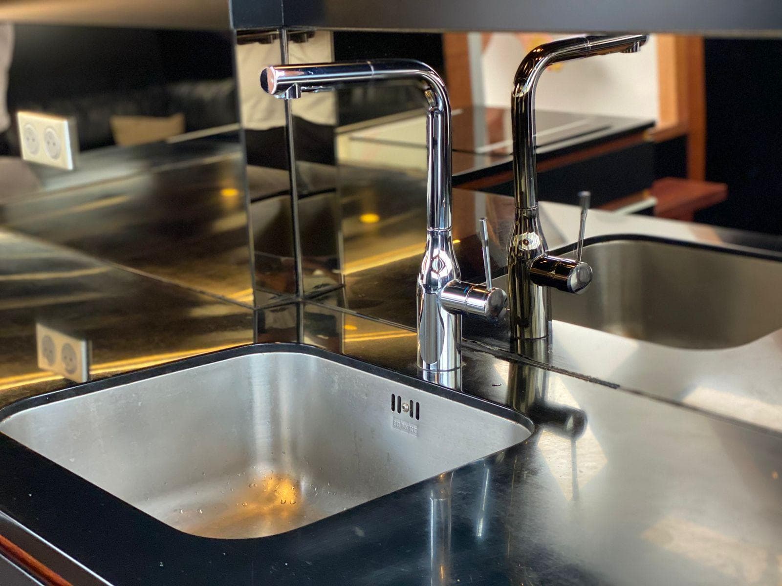 Modern stainless steel sink with dual faucets, reflecting in a mirrored backsplash.