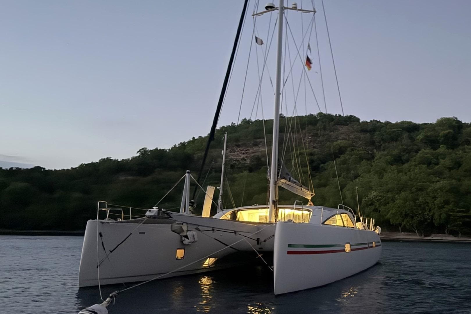 2017 Ice Yachts Ice Cat 61 catamaran anchored at dusk near a forested shoreline.