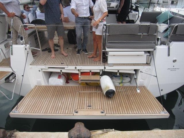 2024 Jeanneau 55 yacht stern with open storage compartments and people on deck.